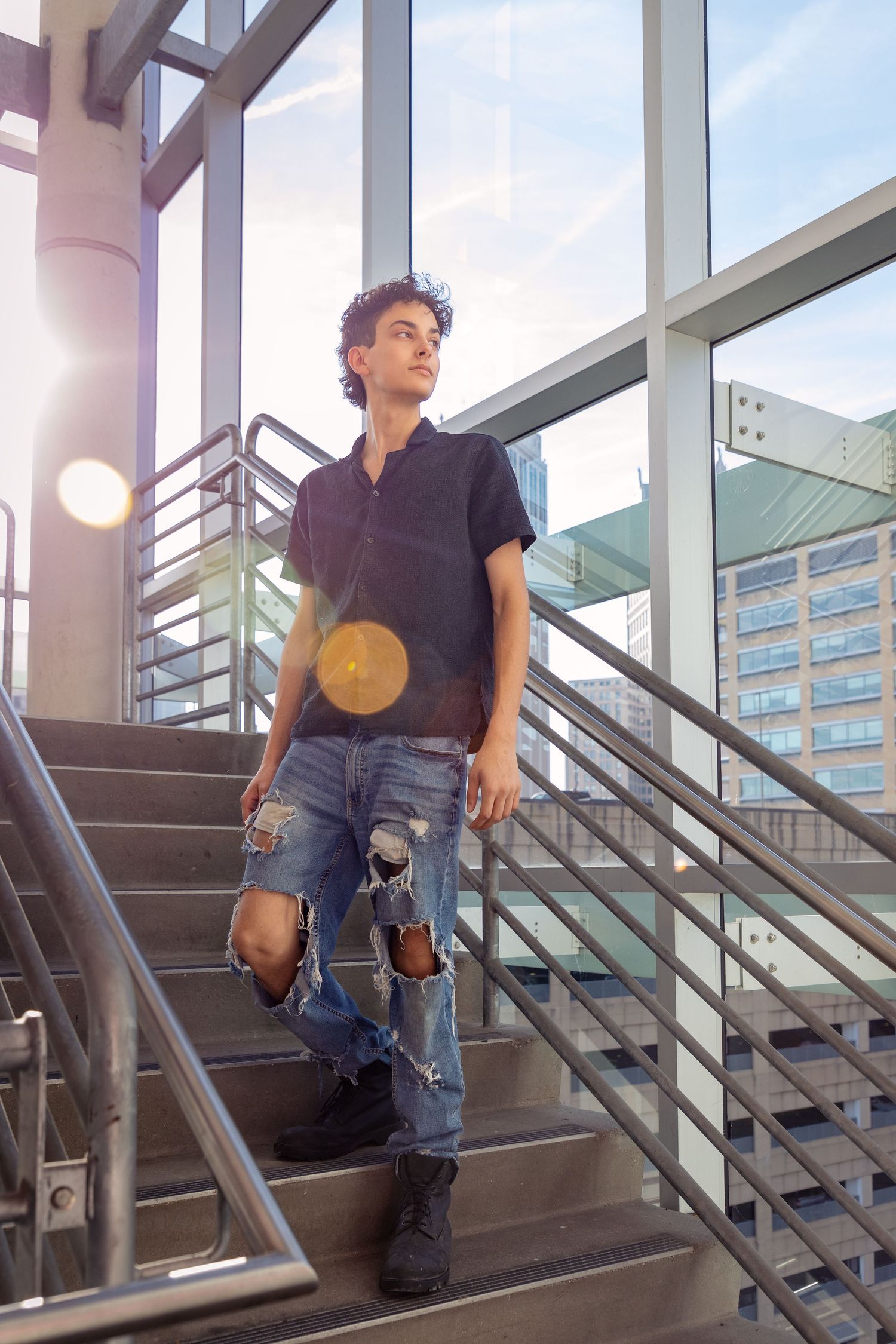 Person in casual wear poses on industrial metal staircase with windows in background.