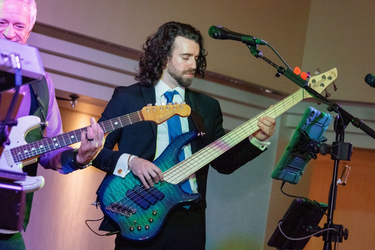 Musicians performing with guitars on stage under colorful stage lighting.