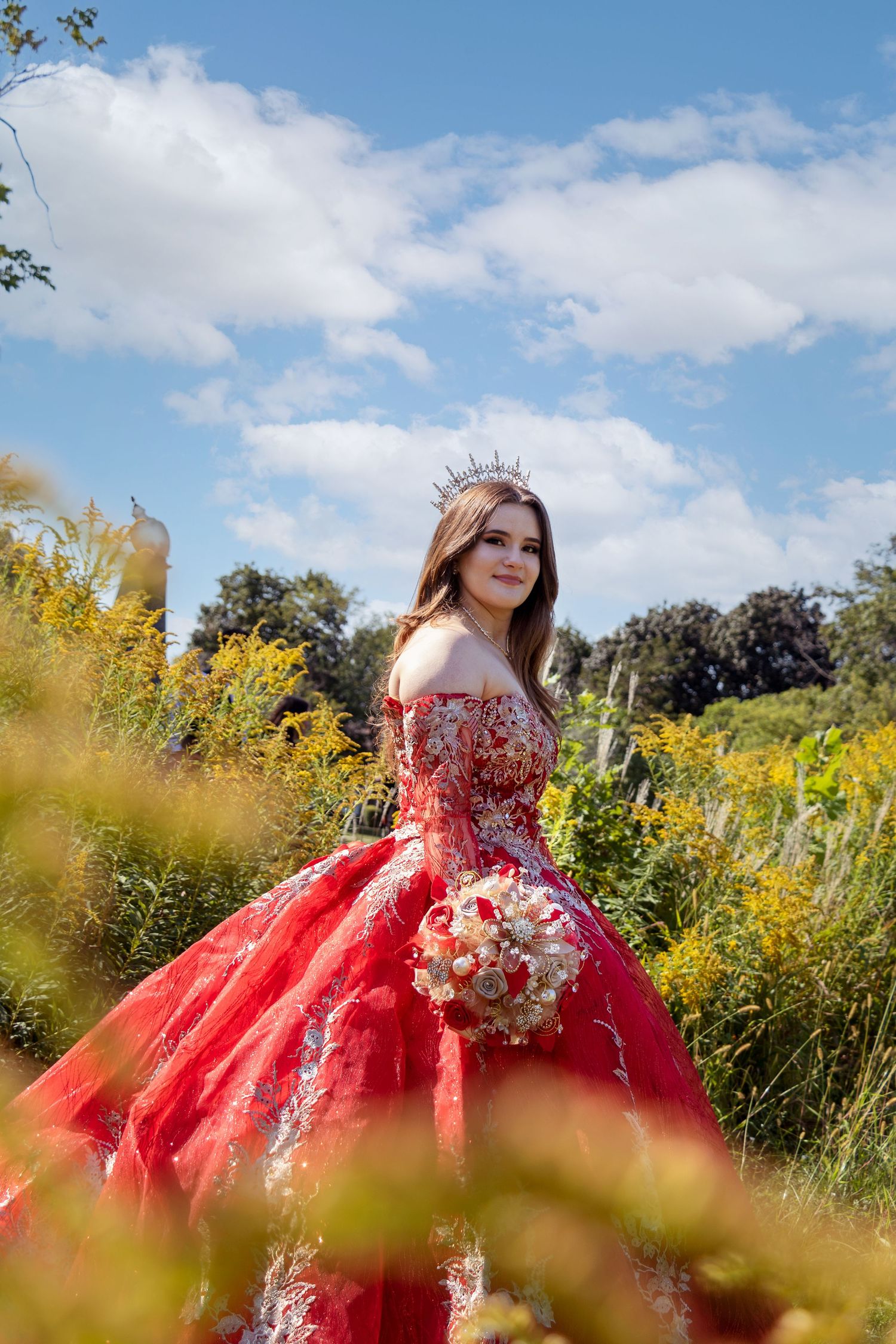 A stunning red ballgown photographed in a field of wildflowers under blue skies.