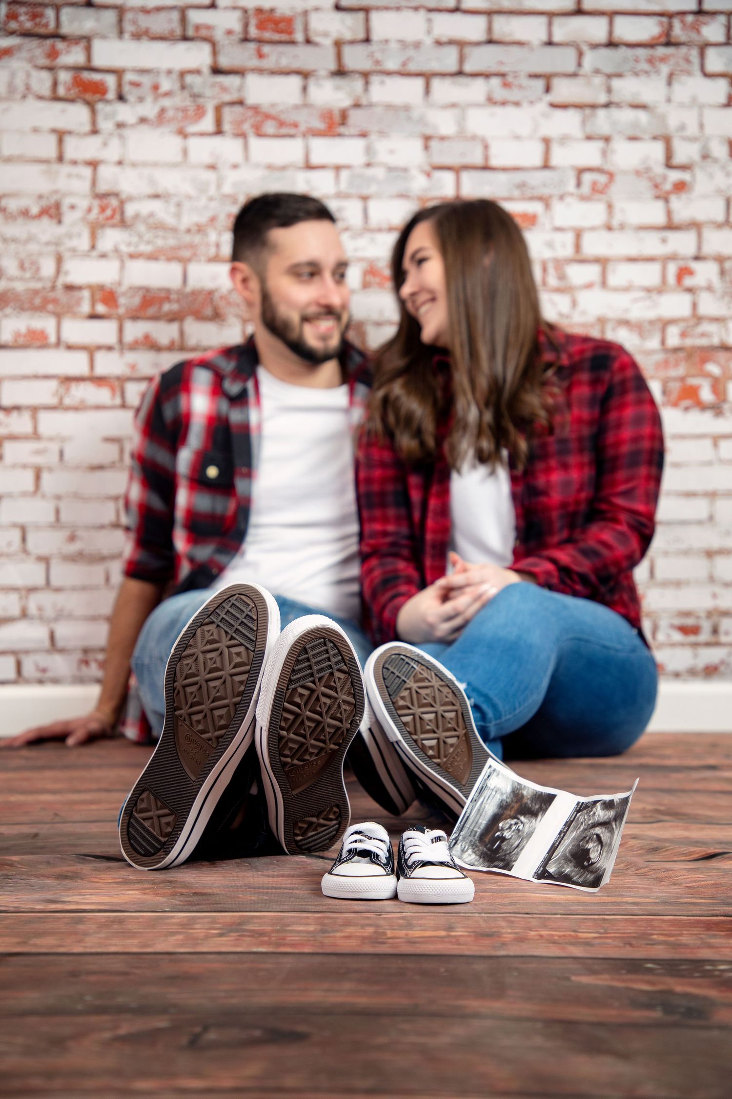 Creative pregnancy announcement with adult shoes and baby shoes arranged with ultrasound photo on wooden floor.