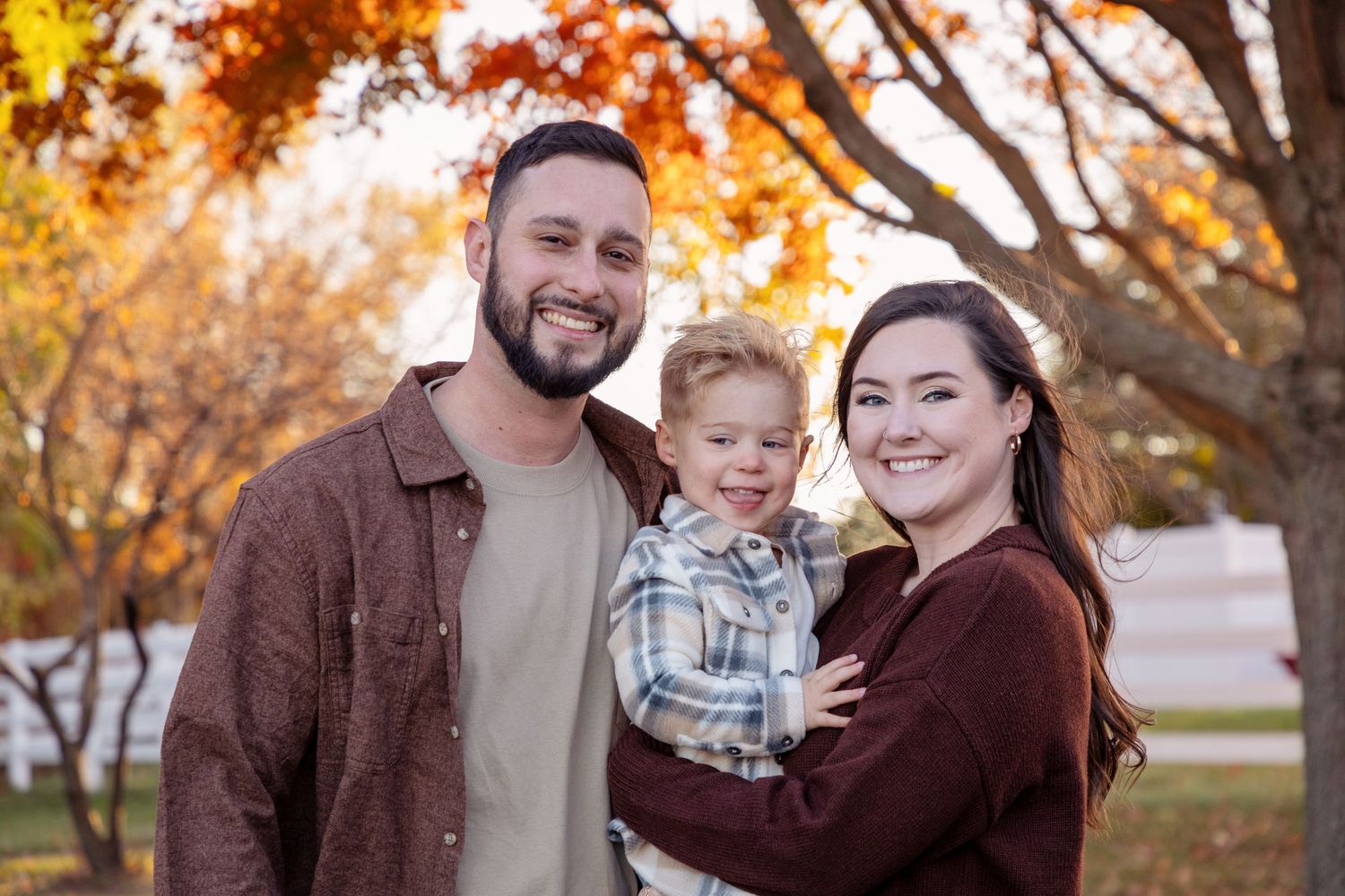 Family autumn portrait session with warm brown tones and golden fall foliage in background.
