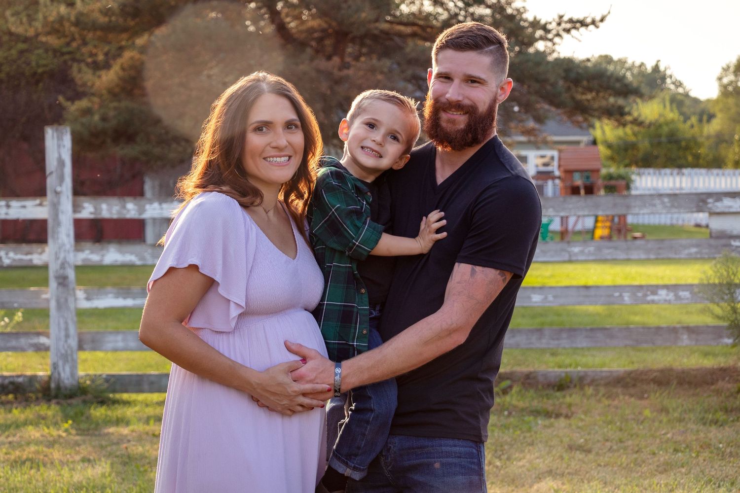 A family maternity photo at sunset with rustic wooden fencing in the background.