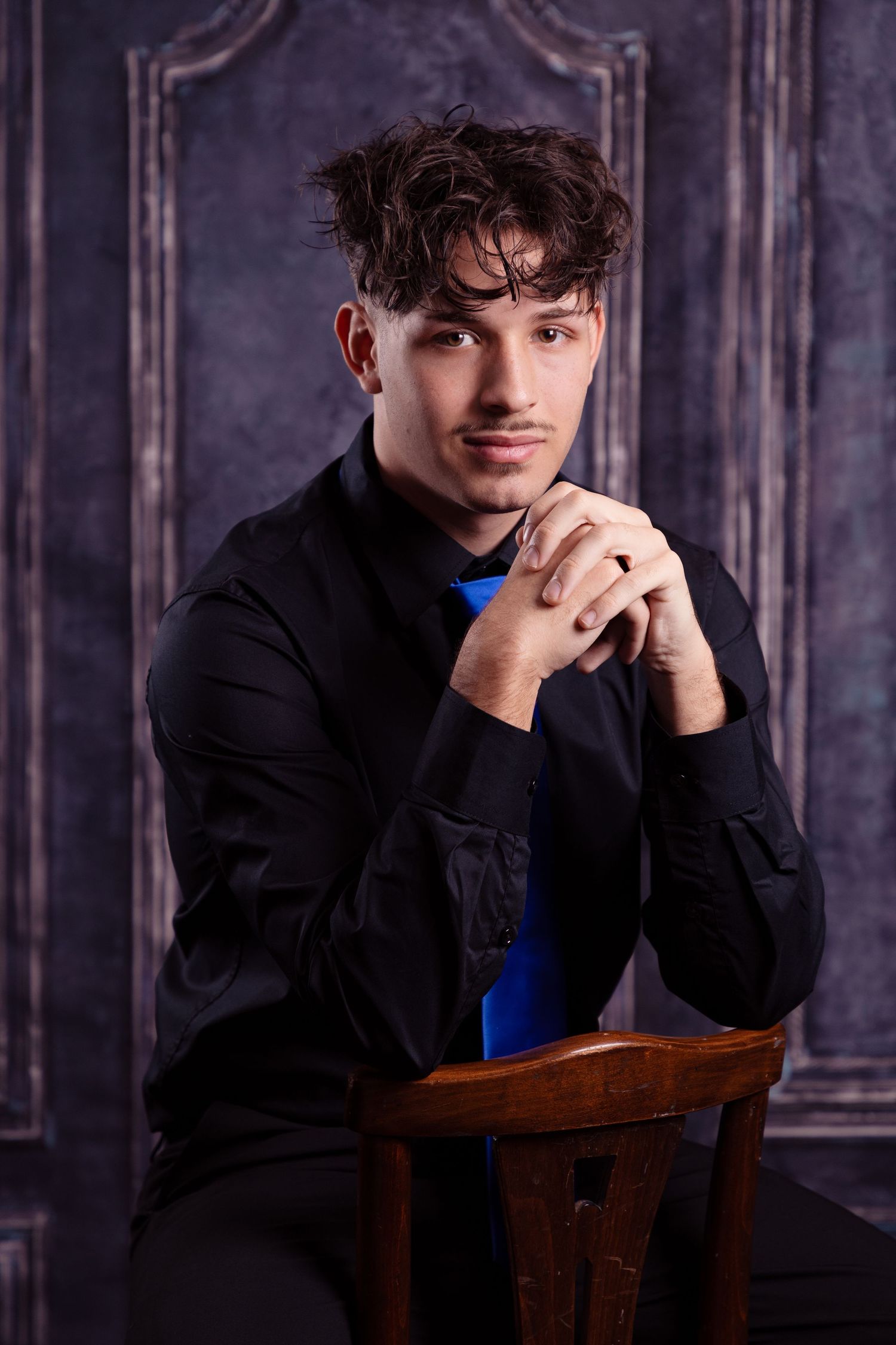 Artistic portrait in dark setting with moody lighting and wooden chair.