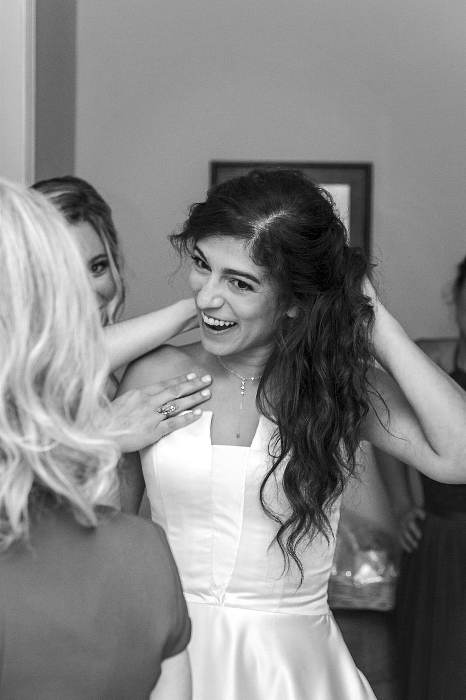 A joyful bride in a white dress laughs while getting ready with her wedding party.