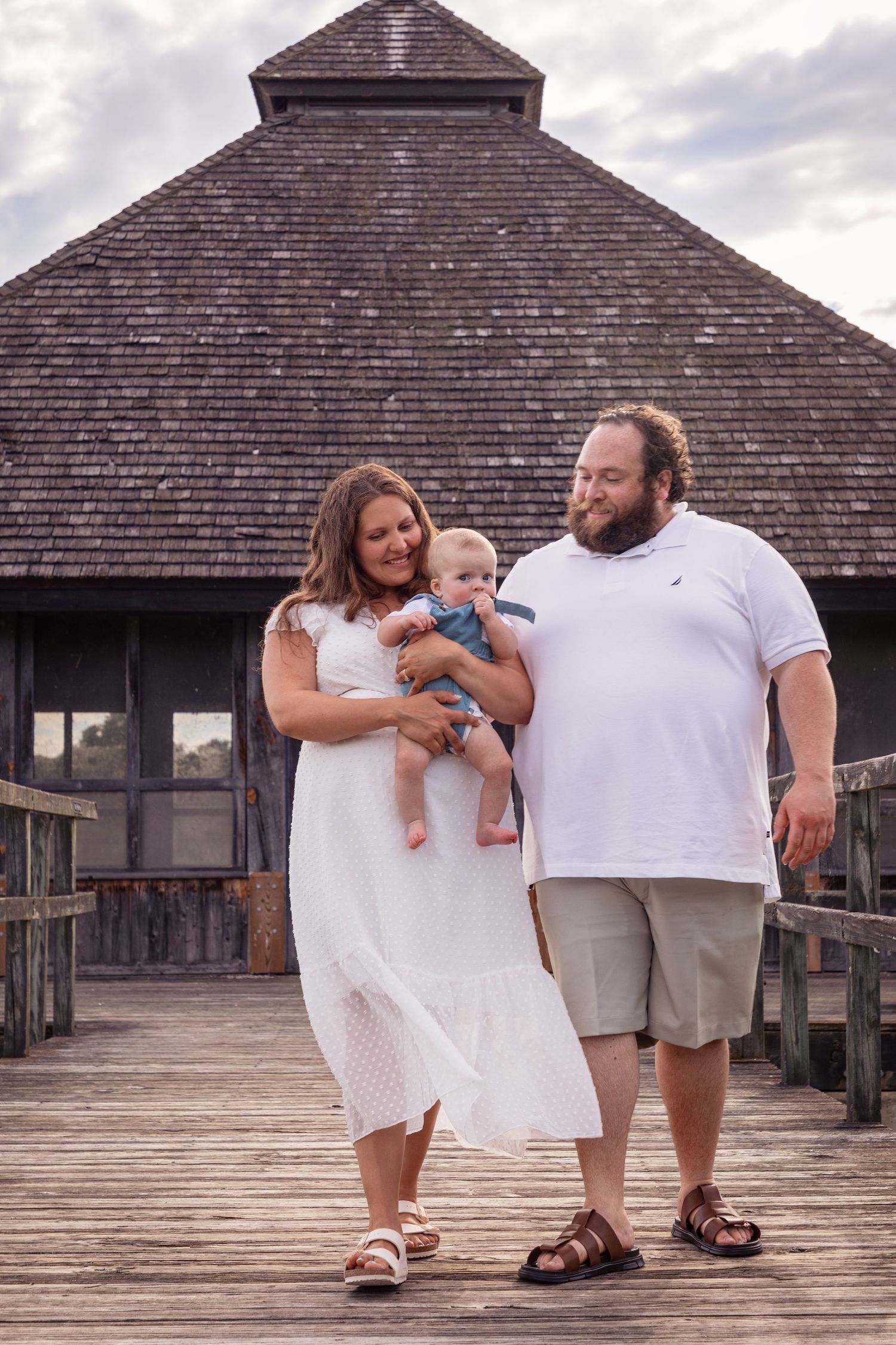 Family posing together on wooden deck structure during cloudy day photoshoot.