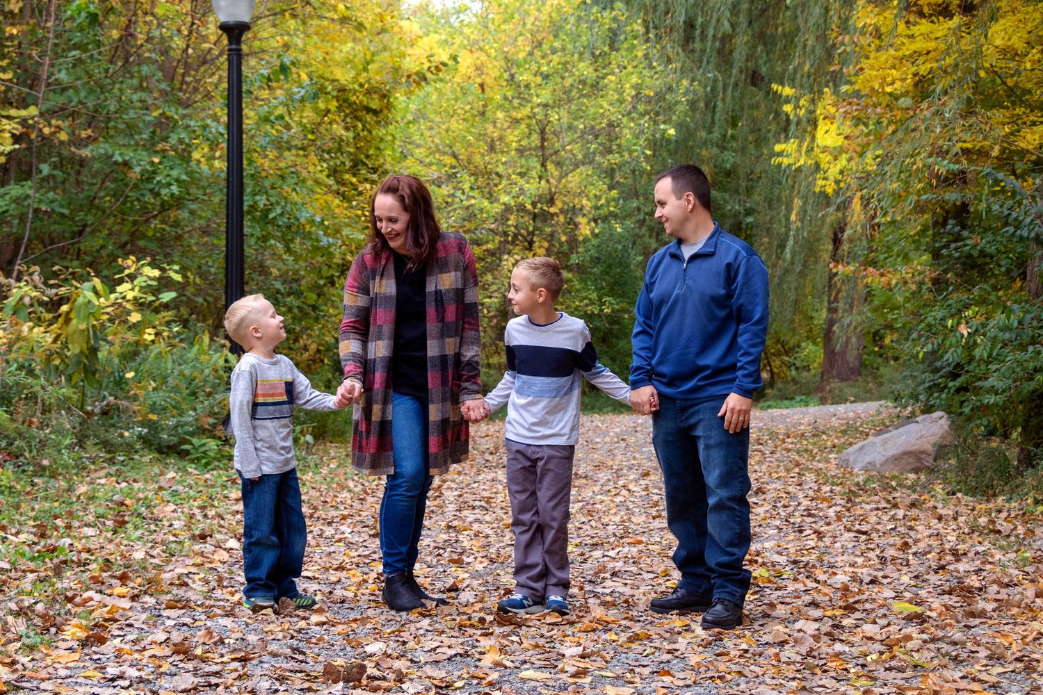 Family walking together on a leaf-covered path in an autumn park setting.