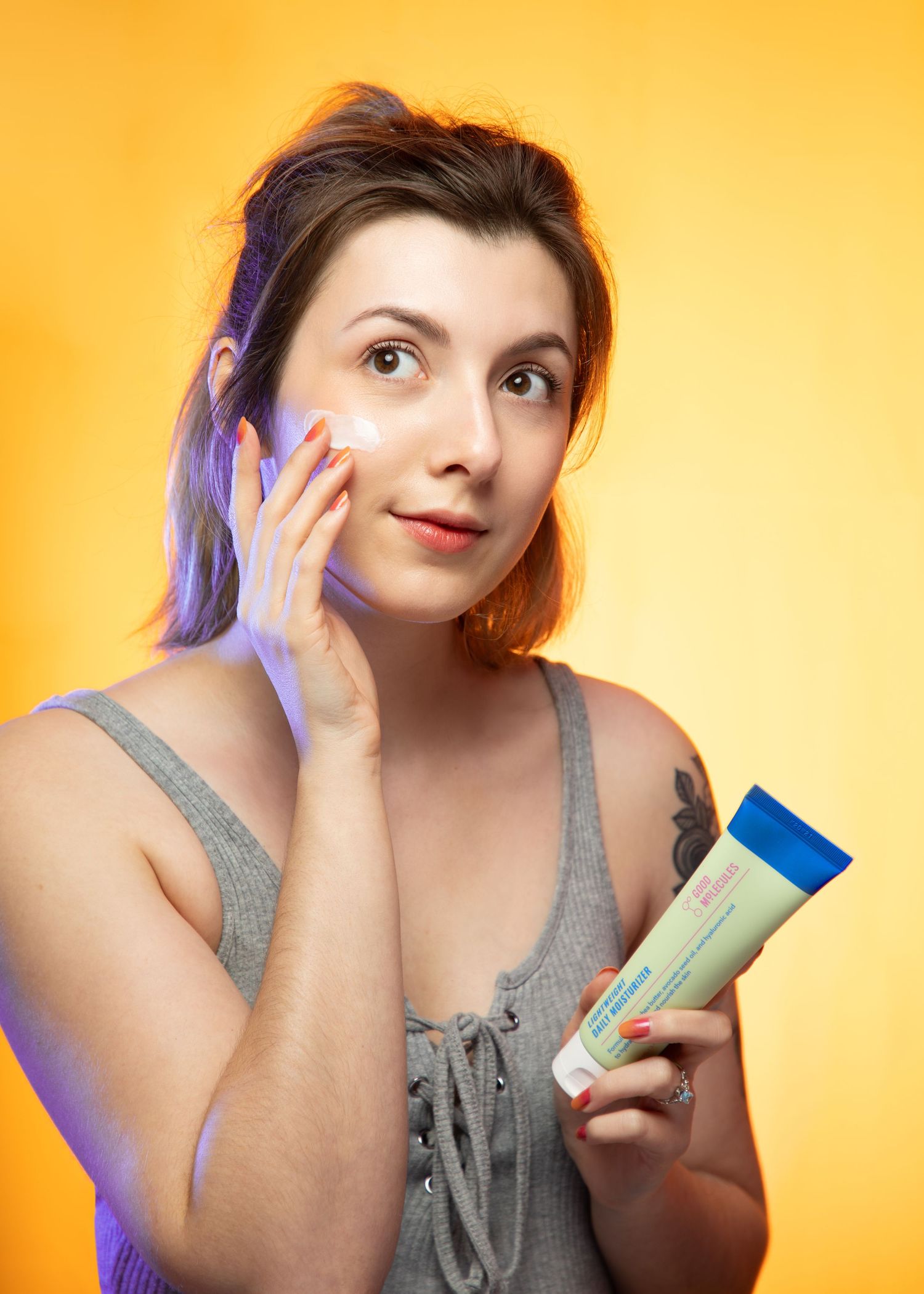 Beauty product demonstration with skincare items against orange backdrop.