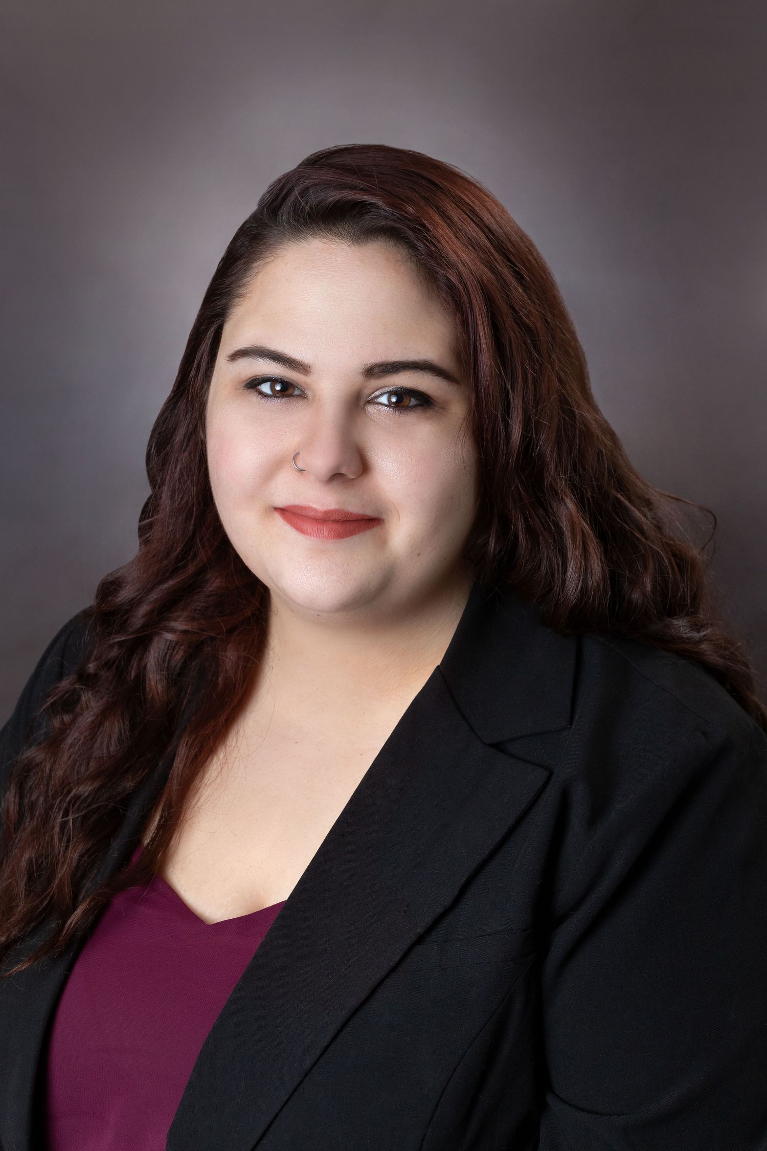 Professional headshot of someone in business attire against a gray studio background.