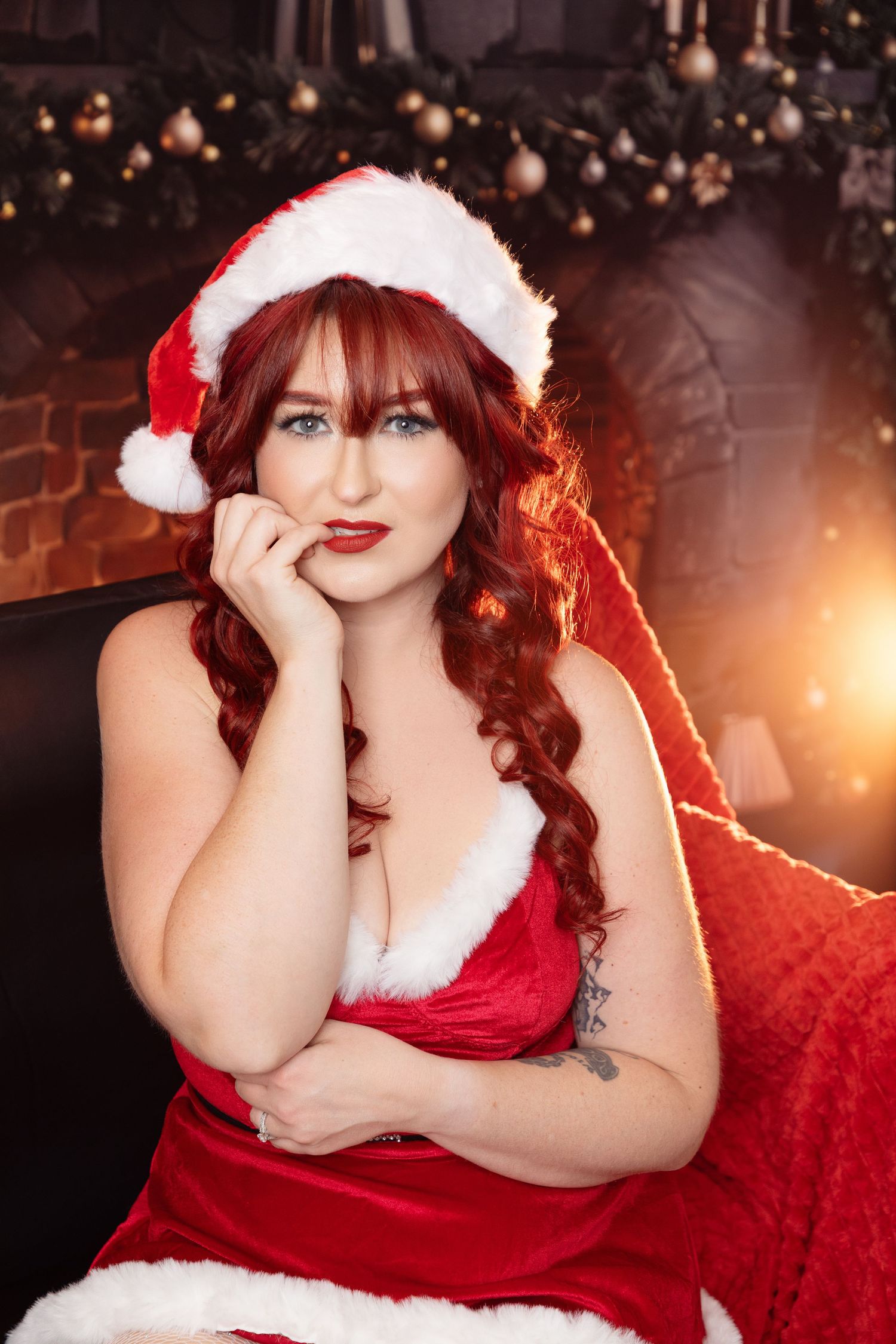 Holiday themed portrait with Santa hat and red velvet dress against Christmas lights.