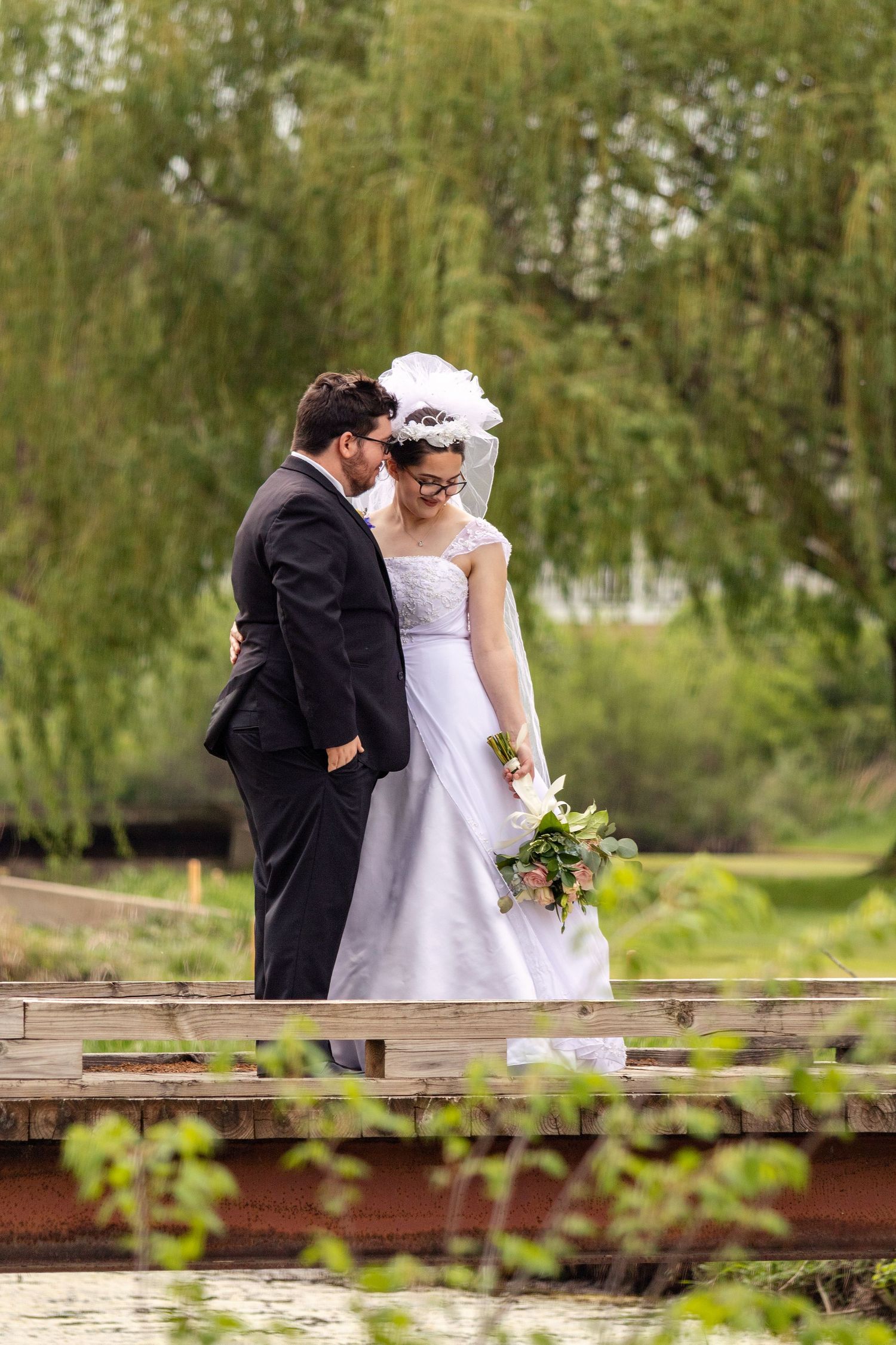 Romantic wedding couple shares intimate moment on wooden boardwalk surrounded by greenery.