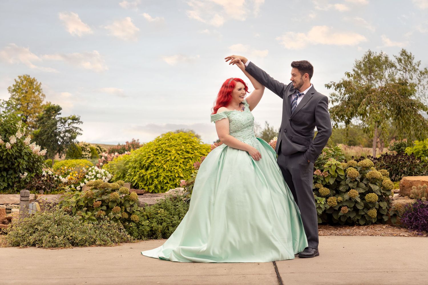 A couple dances together outdoors, with the person wearing a mint green ballgown and their partner in a dark suit.