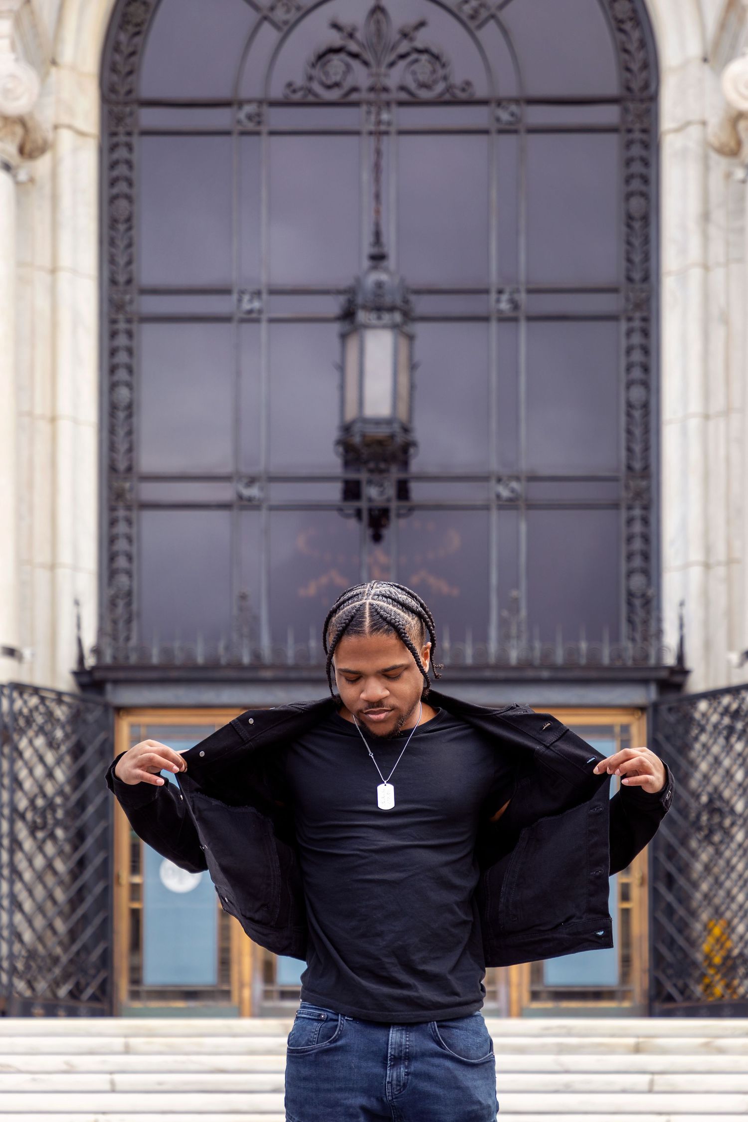 Person in black jacket poses dramatically in front of ornate architectural doorway.