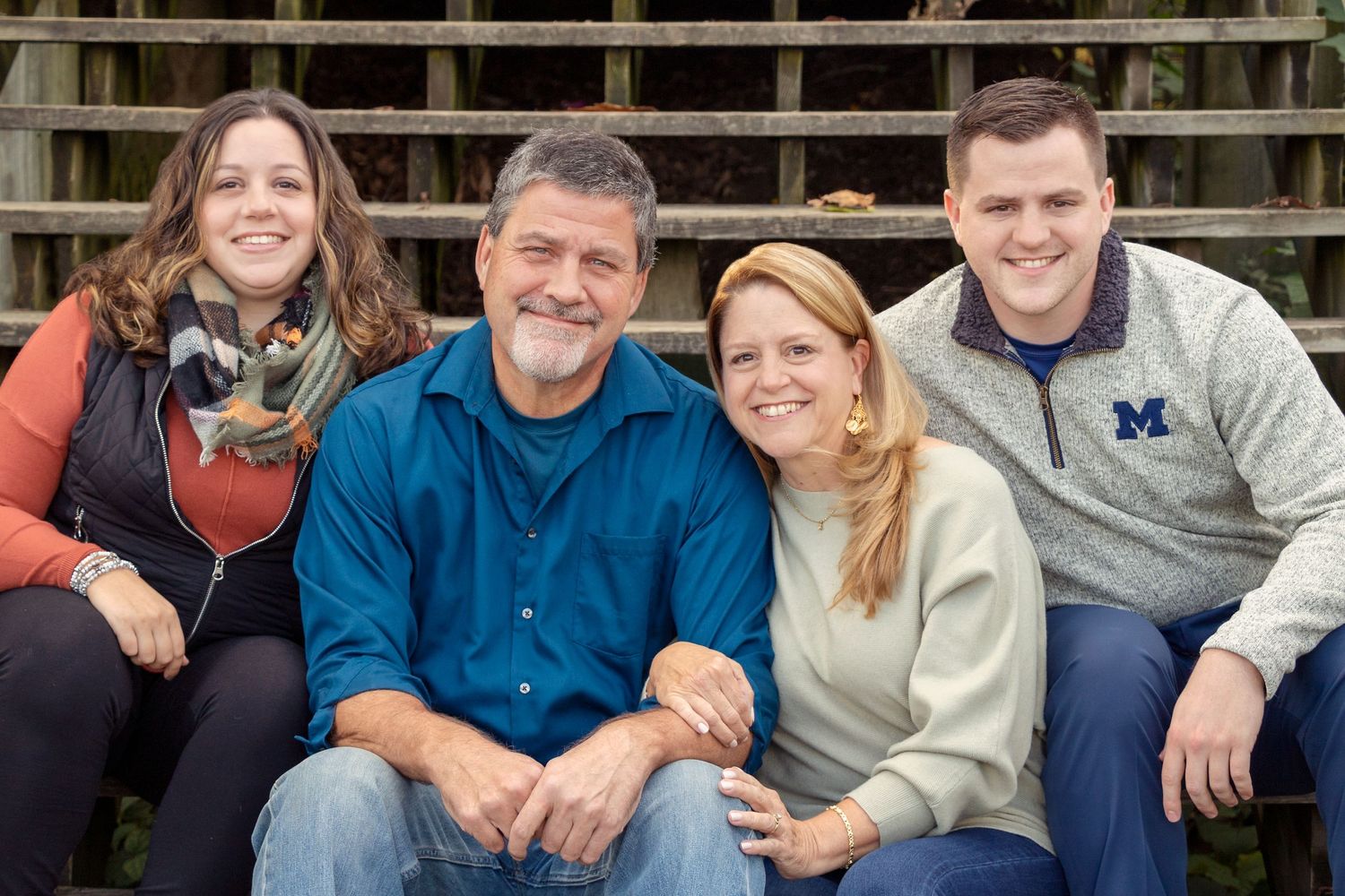 Family group portrait on rustic wooden fence in casual attire.