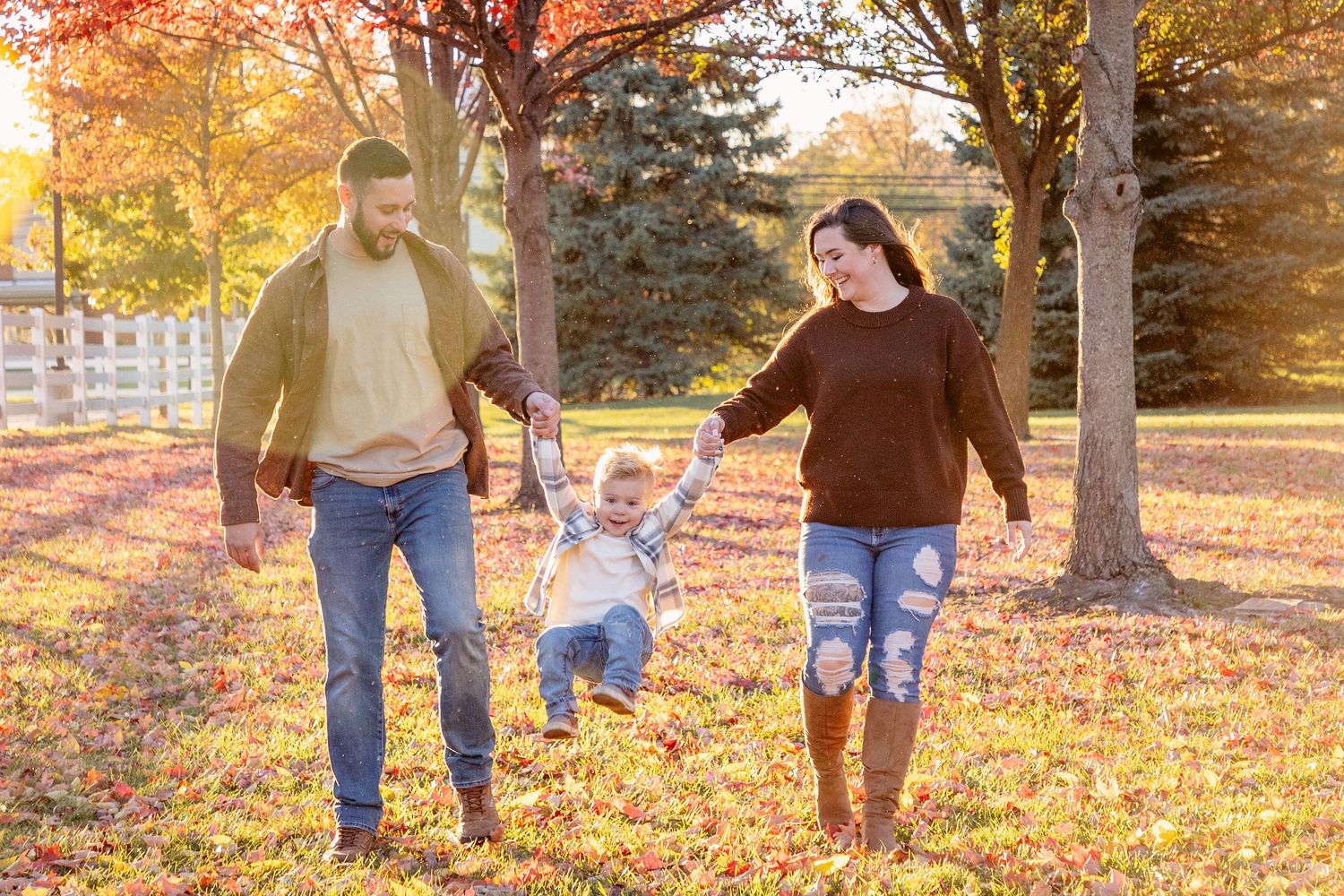 Family playing and walking through fallen autumn leaves in a park at sunset.