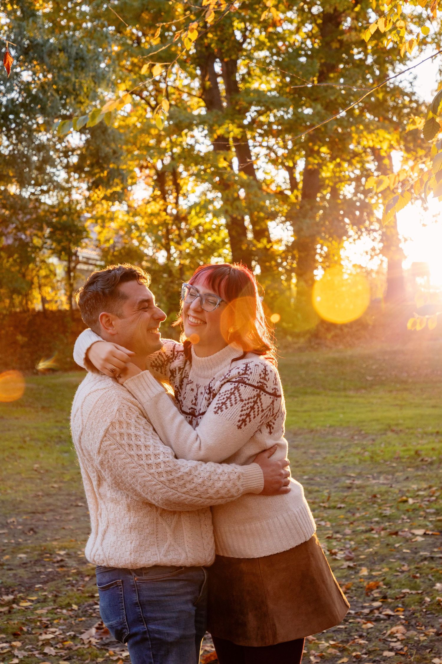 Couple in matching cream sweaters embrace during autumn sunset photo session.