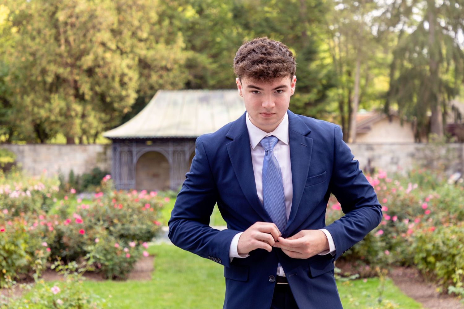 Professional outdoor portraits in navy suit against garden backdrop.