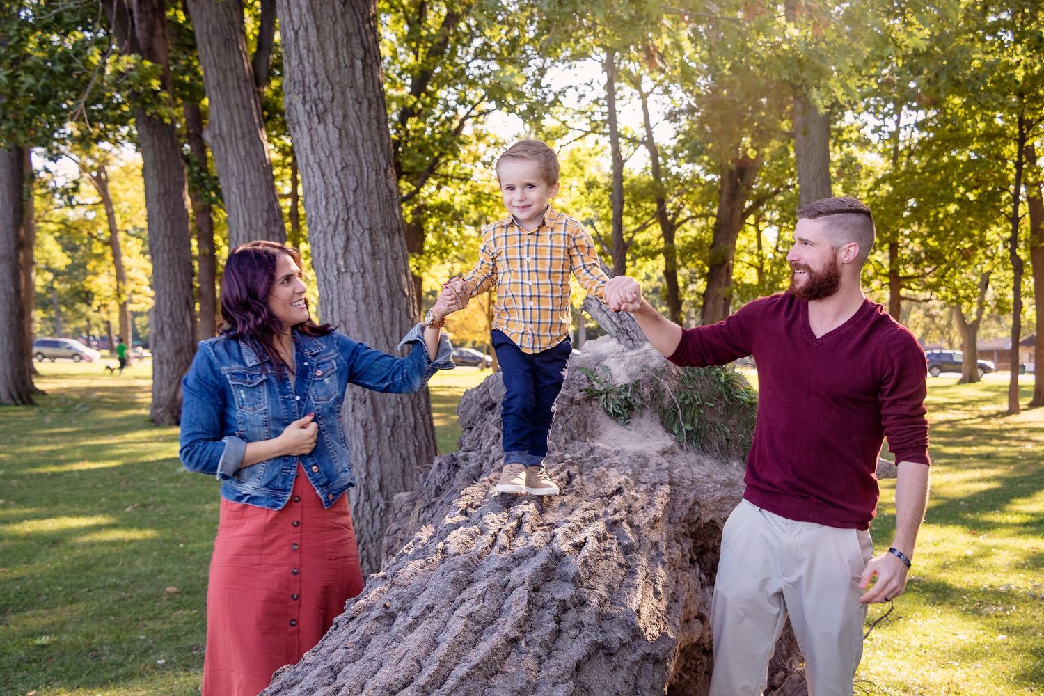 Family sharing intimate moments together in a sunlit park with tall trees.
