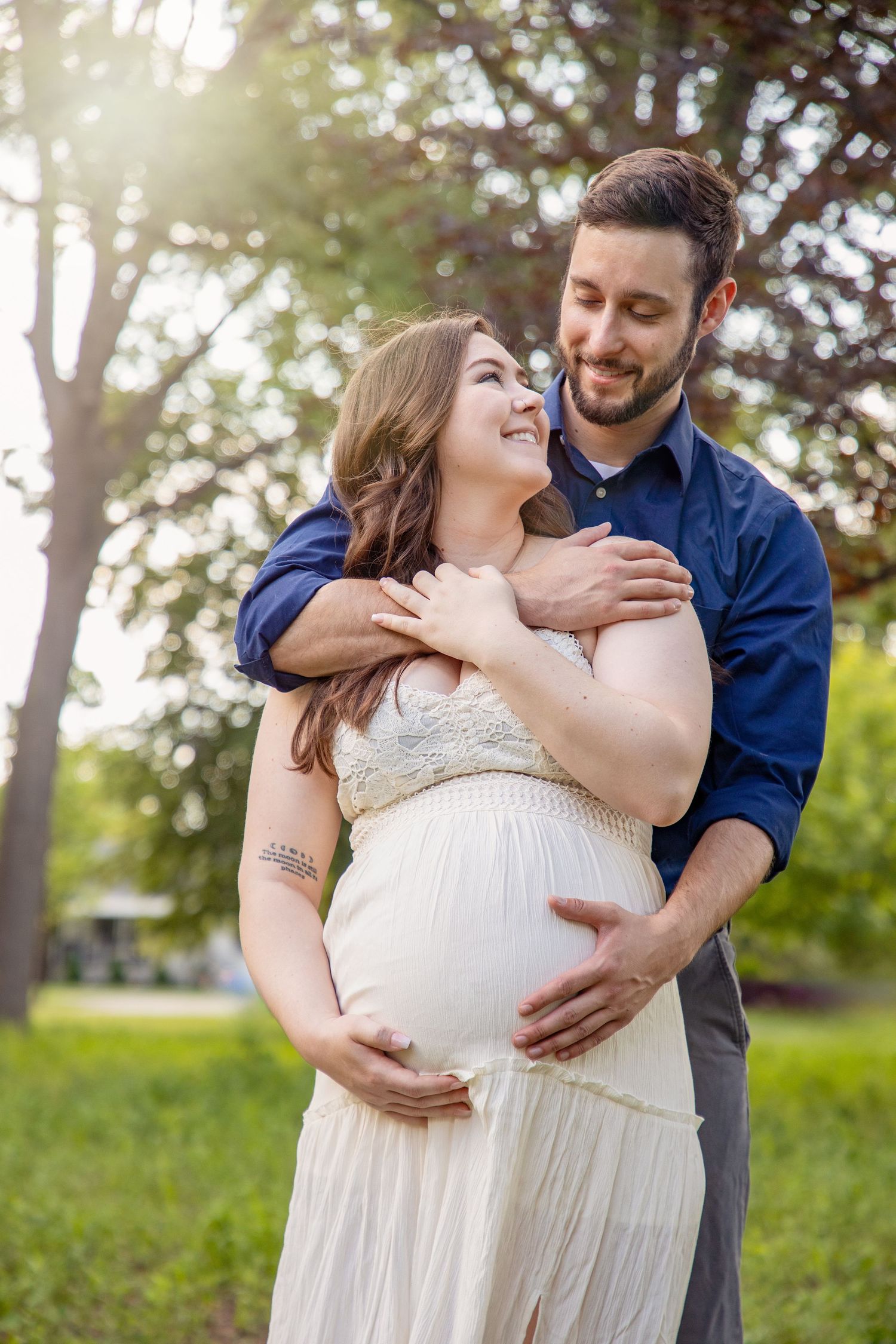 A couple shares intimate moments during an outdoor maternity photoshoot in natural sunlight.