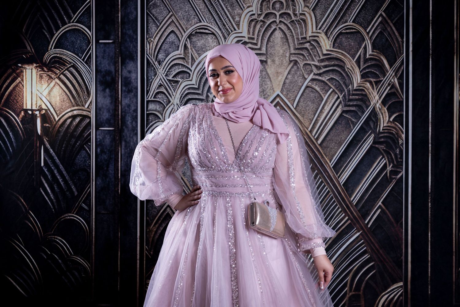 Dreamy portrait session with flowing pink dress against an art deco wall pattern.