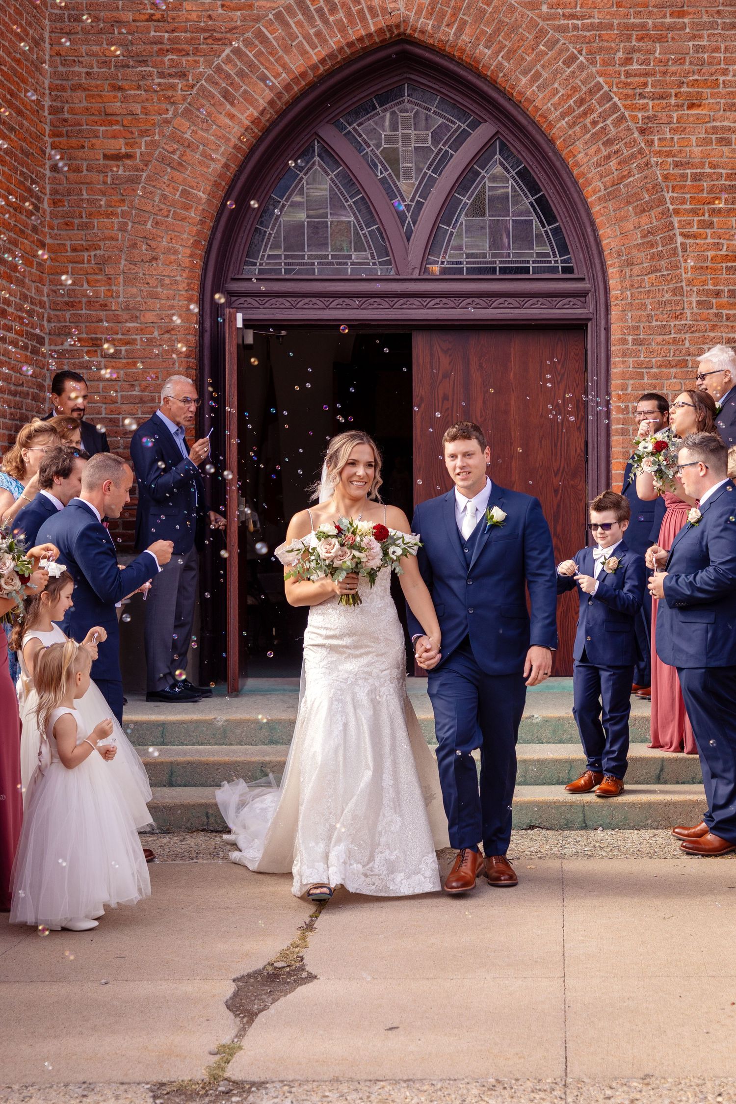 Wedding party exits historic brick church as guests shower them with confetti on the steps.
