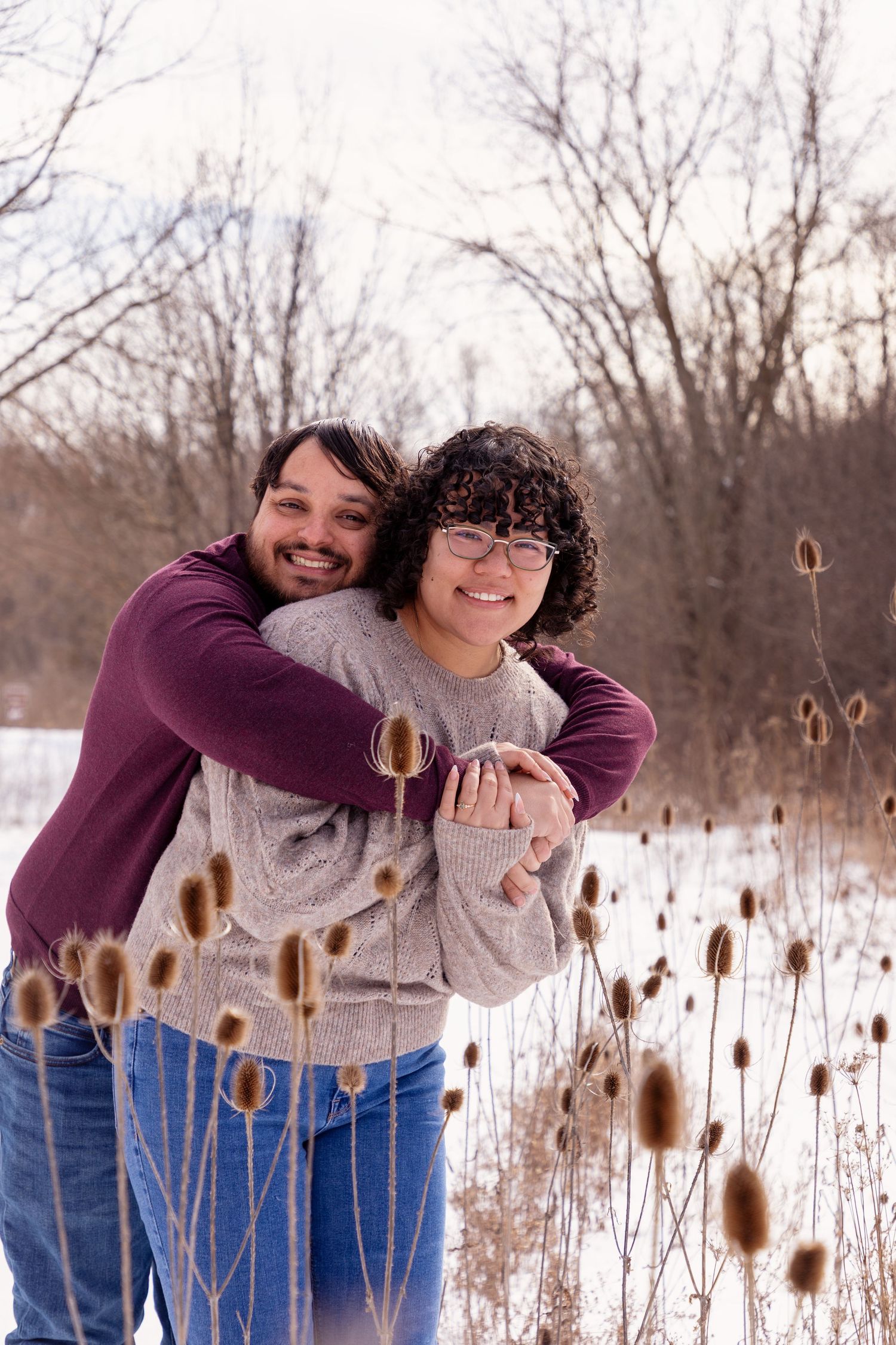 Playful winter engagement photos among cattails in snowy field.