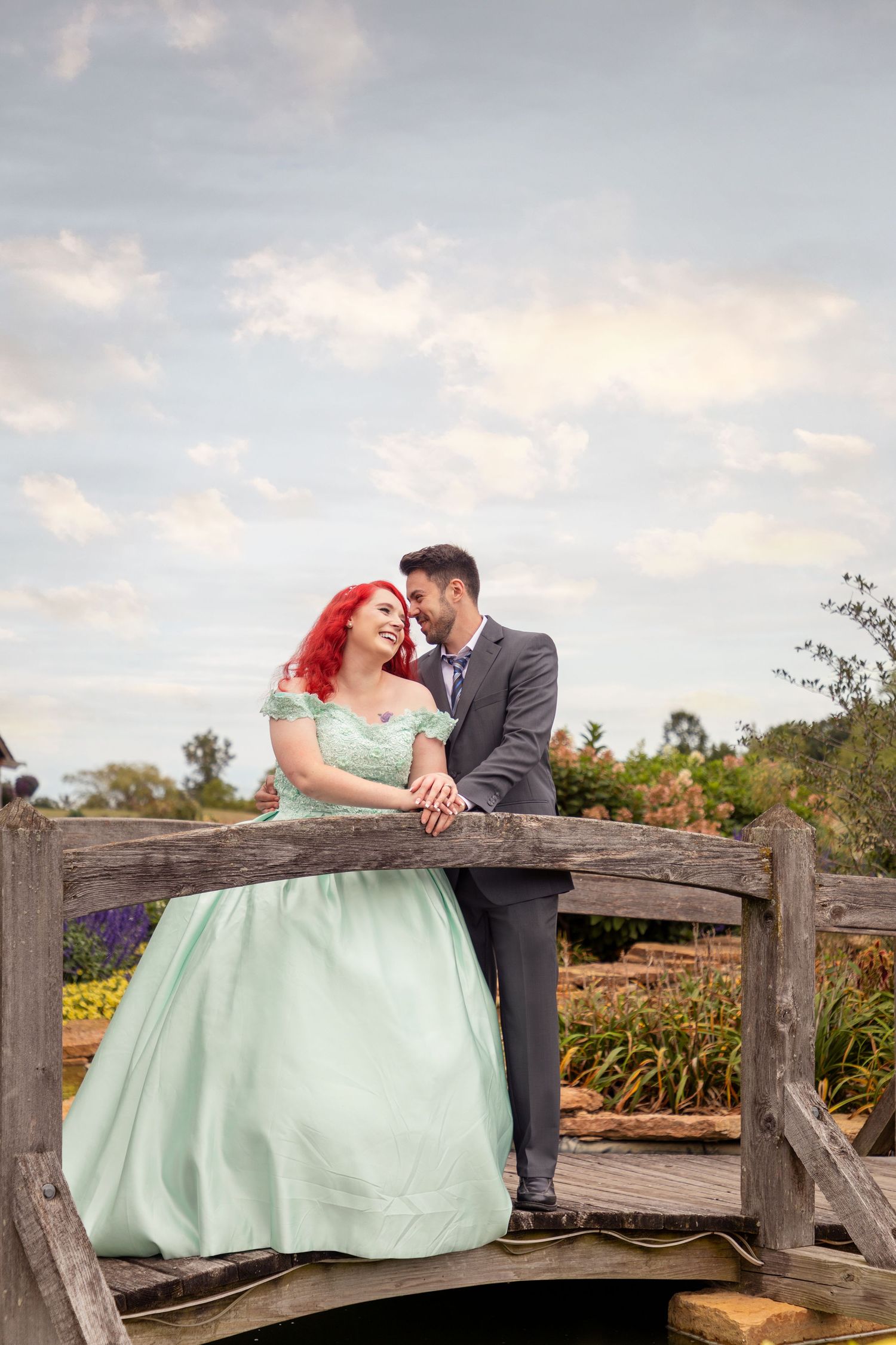 A couple shares a romantic moment on a rustic wooden bridge against a cloudy sky.