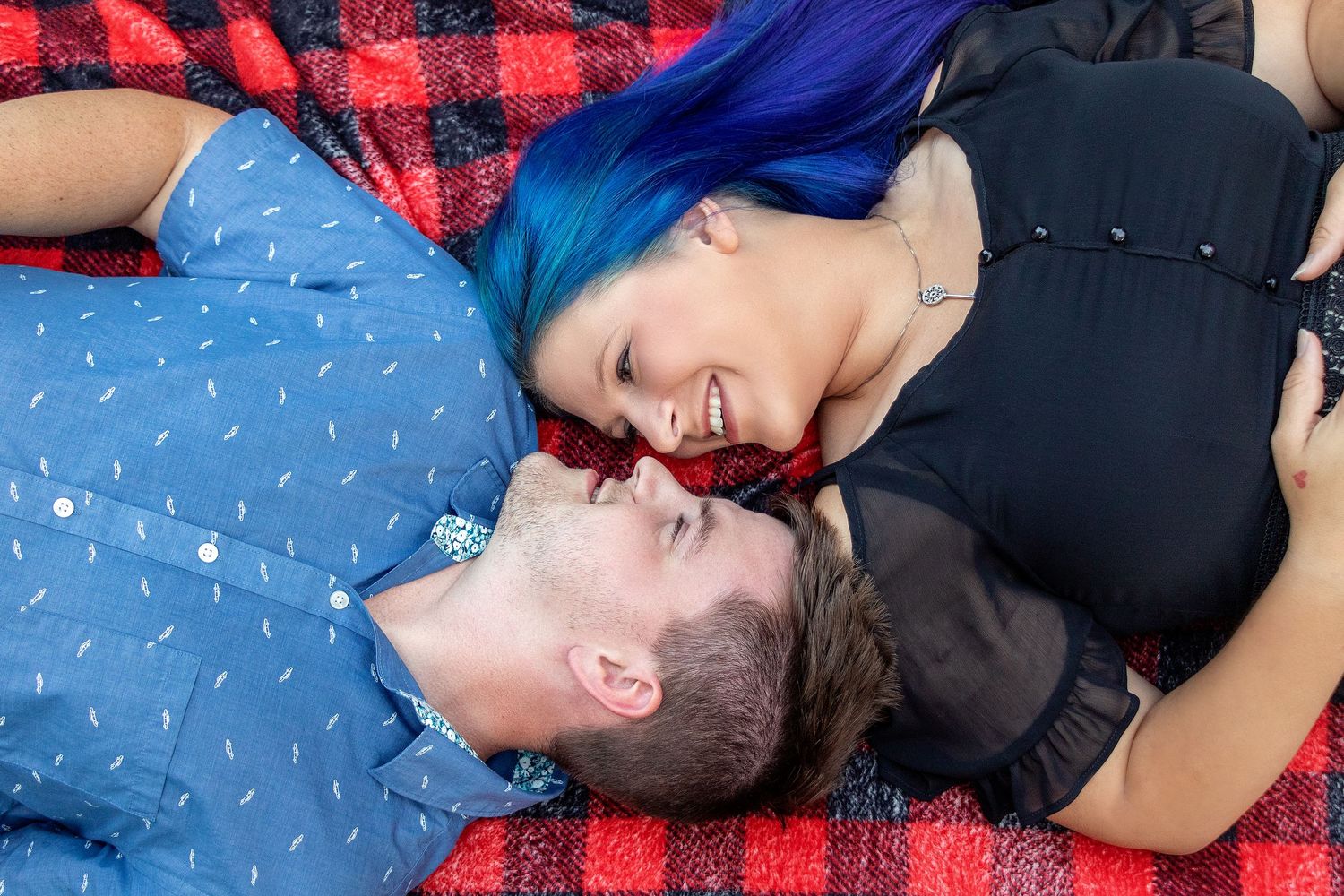 A couple lying on a red plaid blanket share a tender moment together.