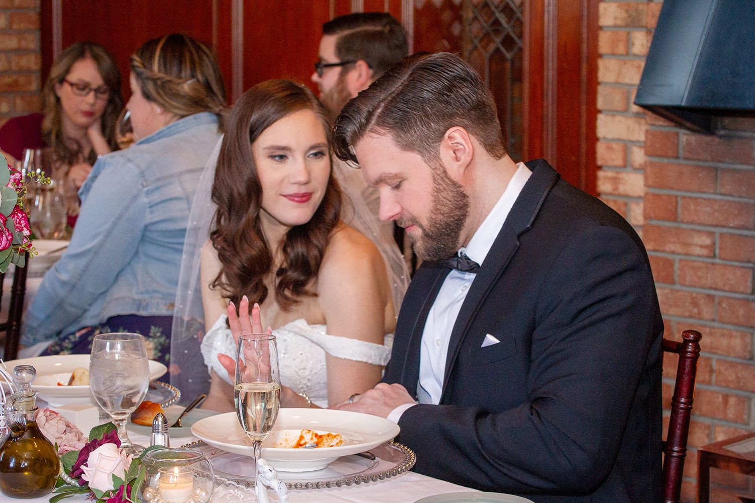A wedding couple sits together at their reception dinner table.