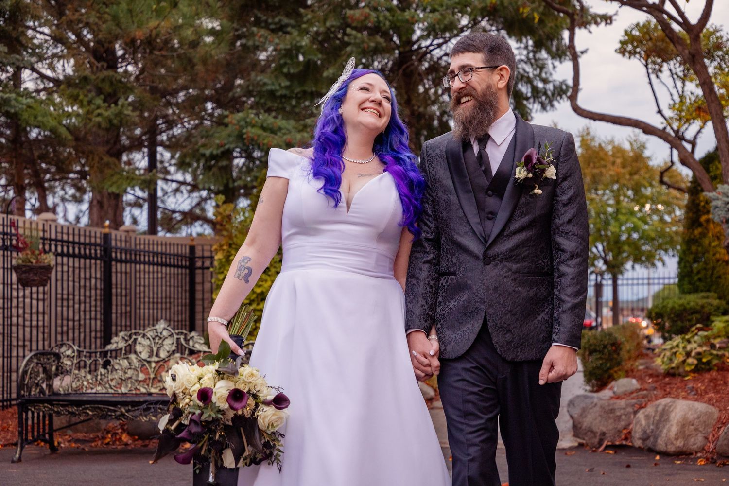 Couple walks hand in hand through autumn garden pathway on their wedding day.