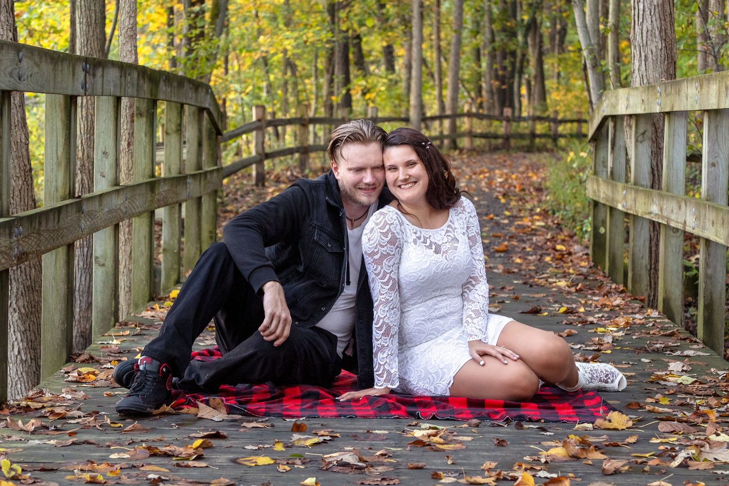 A couple relaxes on a wooden bridge covered in autumn leaves.