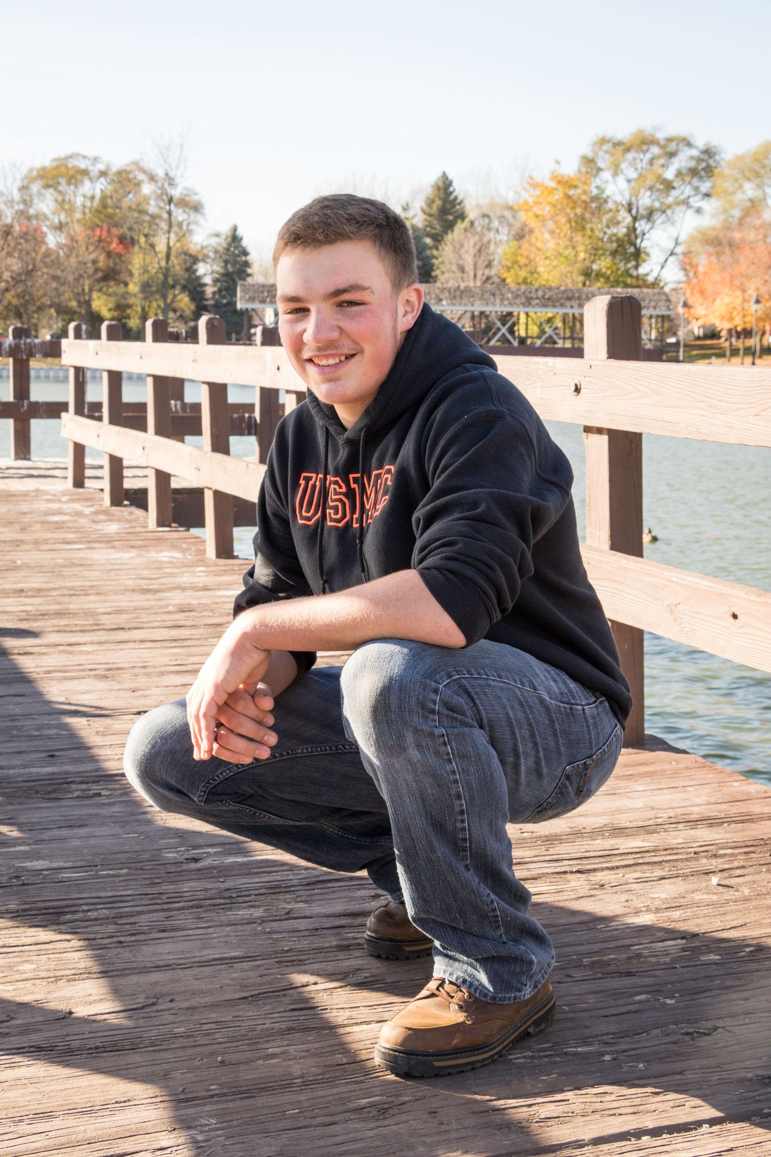 Person in casual wear sits on wooden dock overlooking autumn lake.
