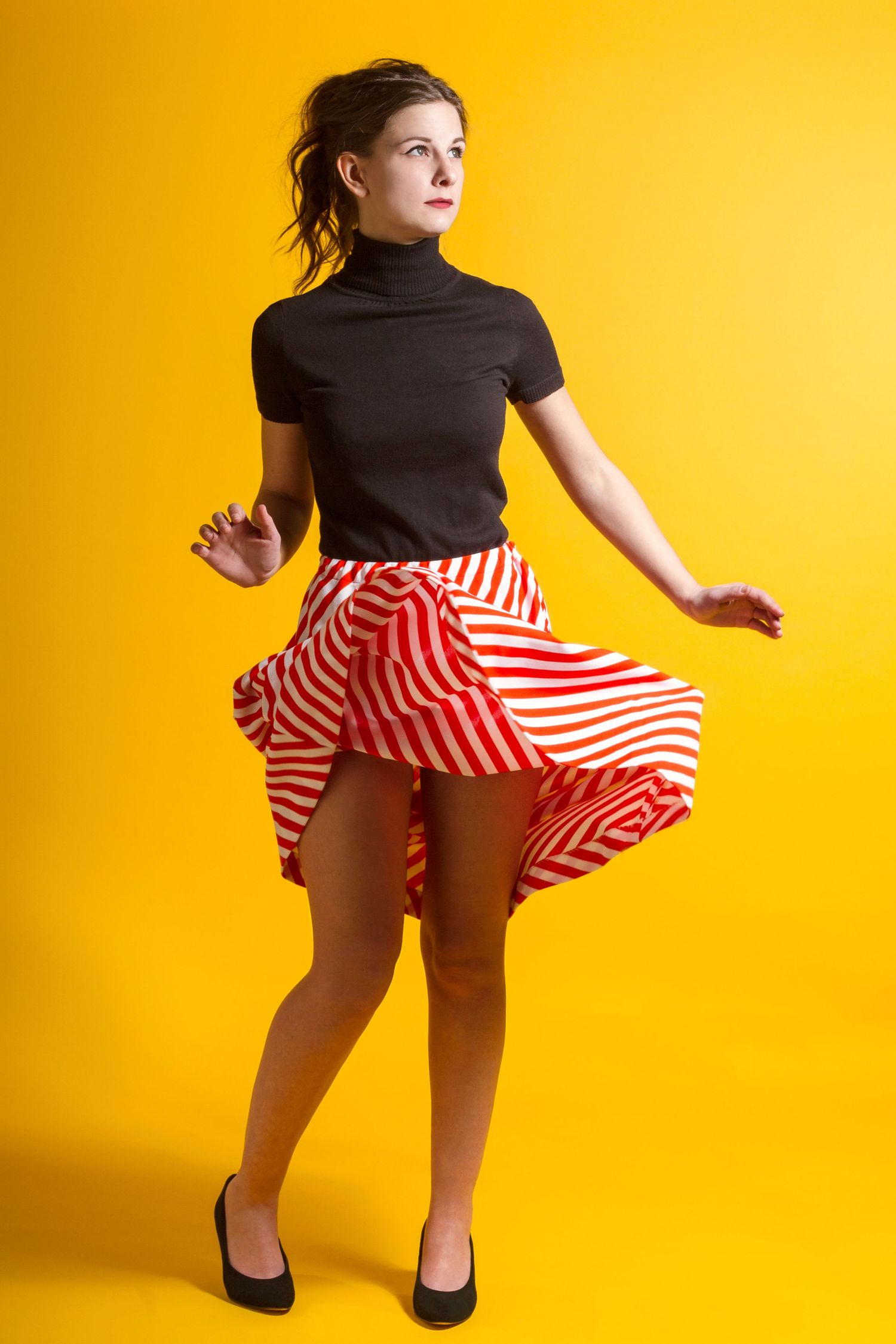 Dynamic poses in black top and red striped skirt against bright yellow background.