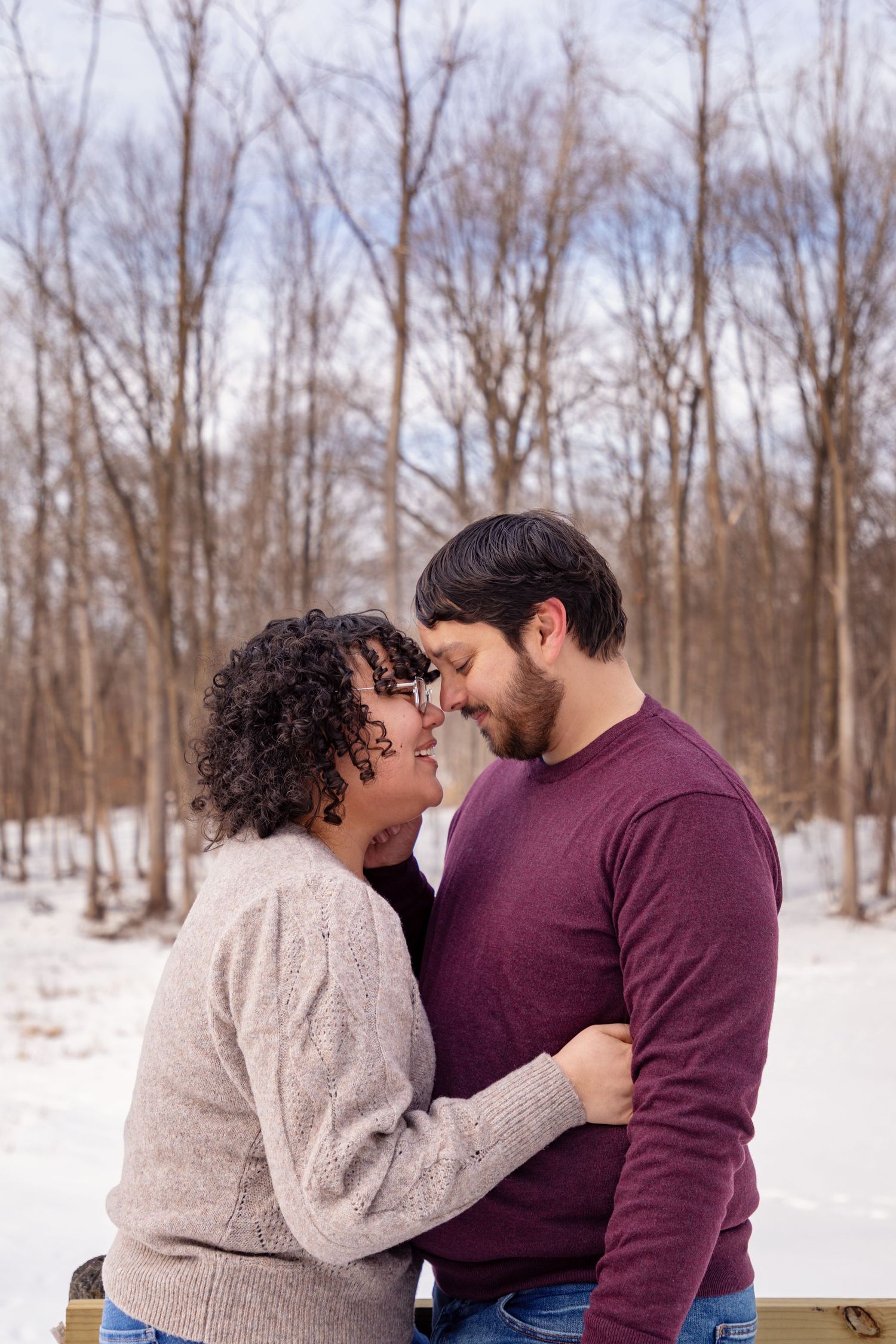 Intimate winter portrait of a couple embracing in a snowy forest setting.