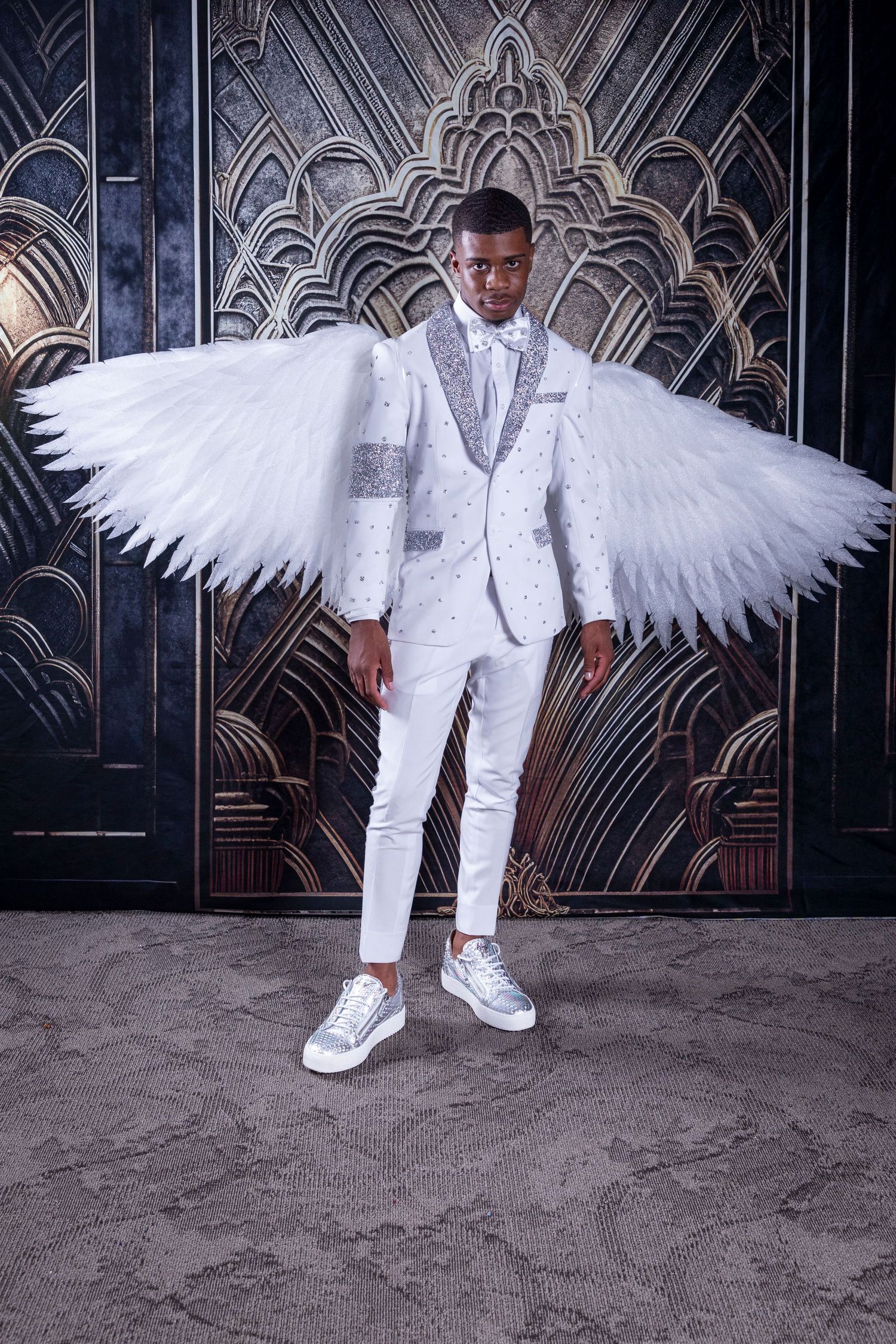 Dramatic portrait with white angel wings and matching white outfit against geometric backdrop.