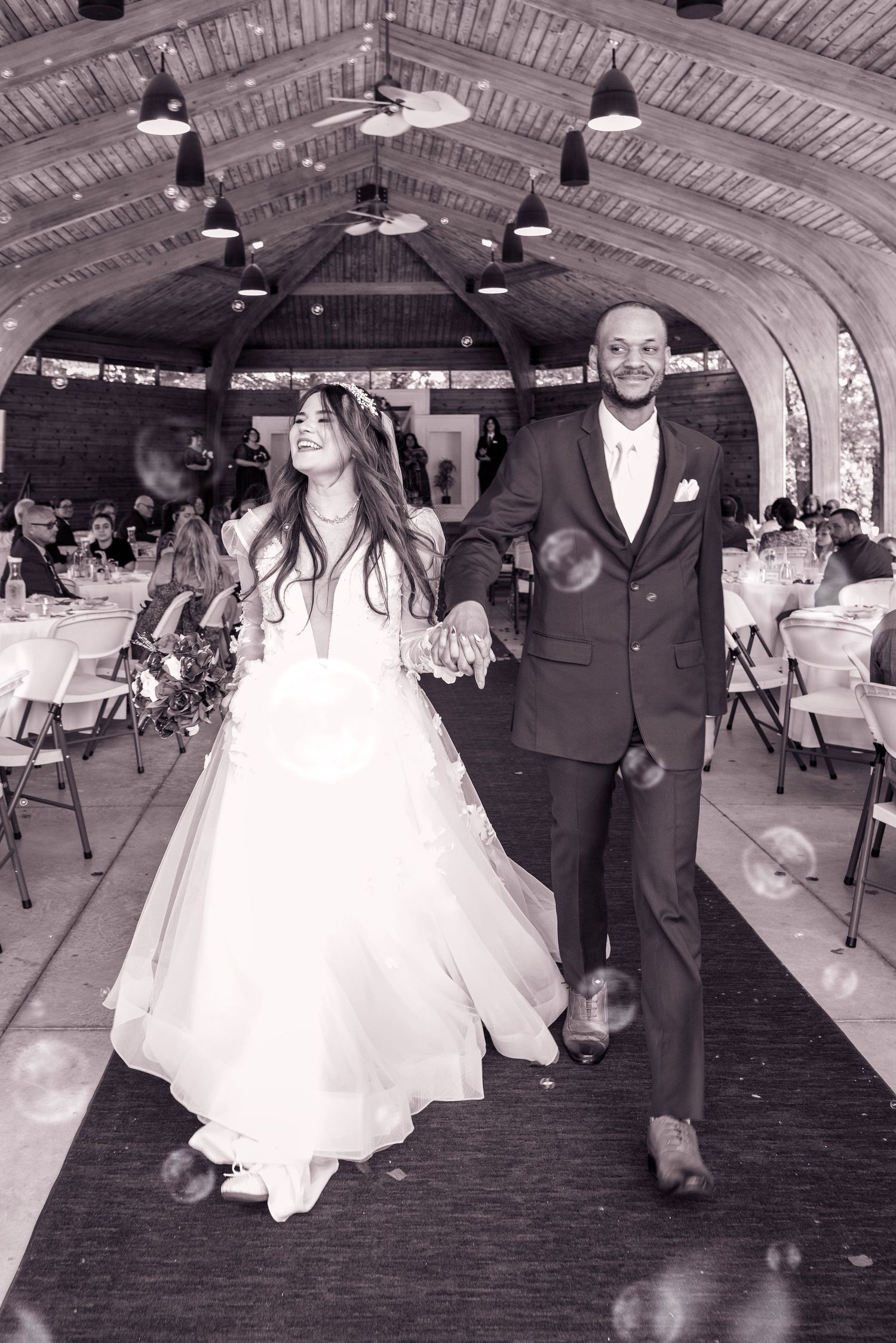 A newlywed couple joyfully exits their wedding reception in a rustic venue.
