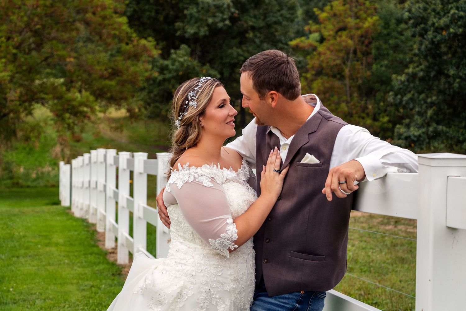 A couple shares an intimate moment by a white picket fence on their wedding day.