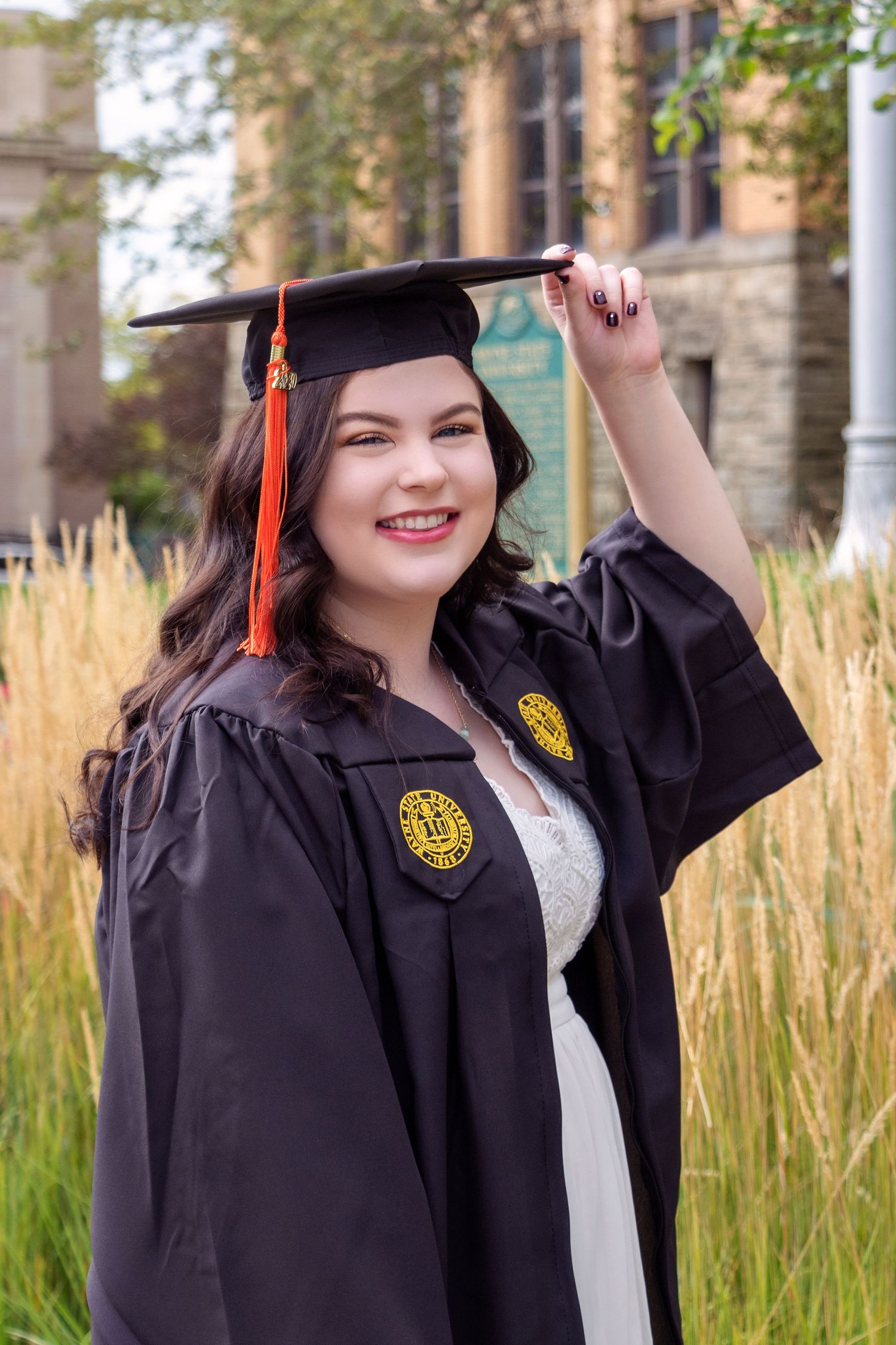 Graduate in black cap and gown celebrating against natural grass background.