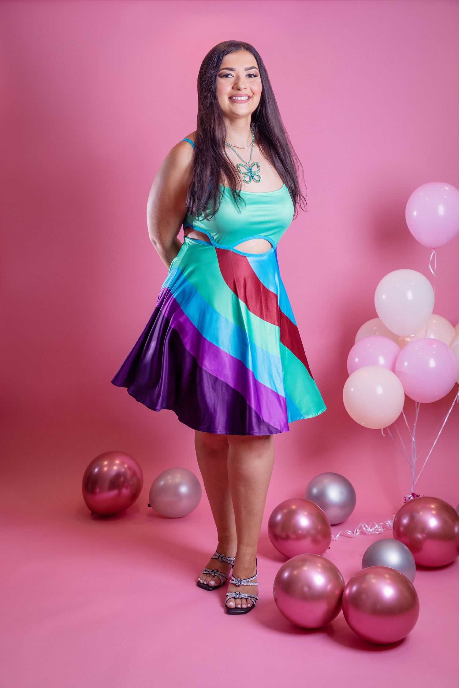 A colorful striped dress with turquoise and purple tones photographed against a pink backdrop with balloons.