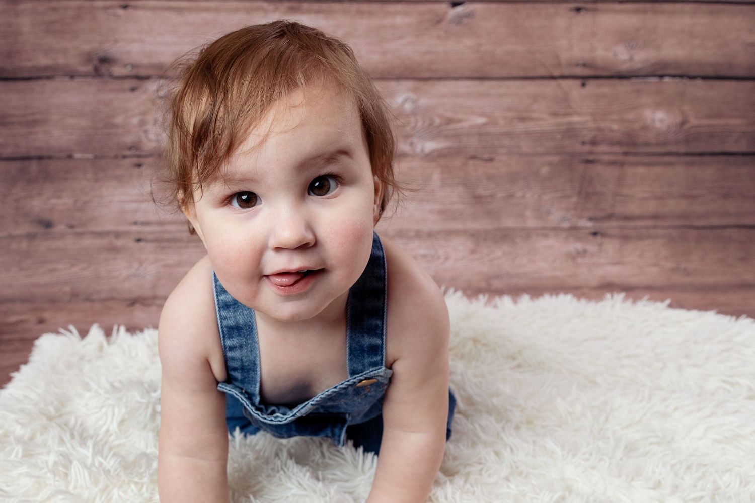 Baby in denim overalls crawling on white fluffy rug in progressive photo sequence.