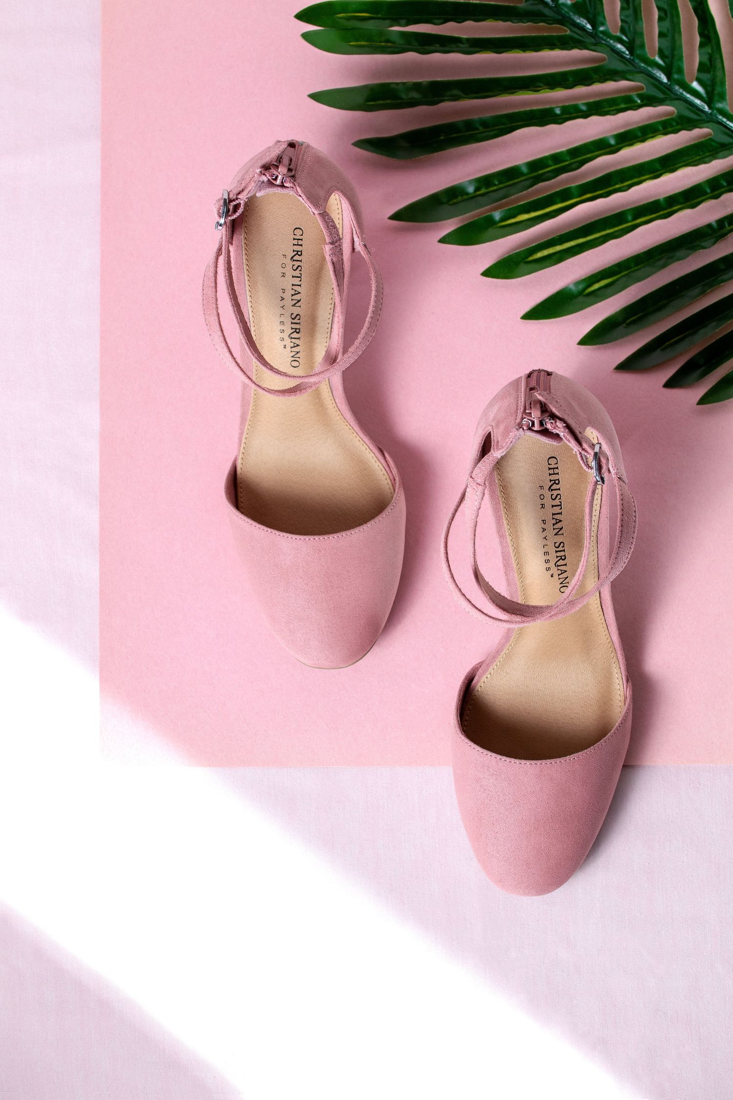 Pink women's ankle strap flats styled with tropical palm leaves on pastel background.