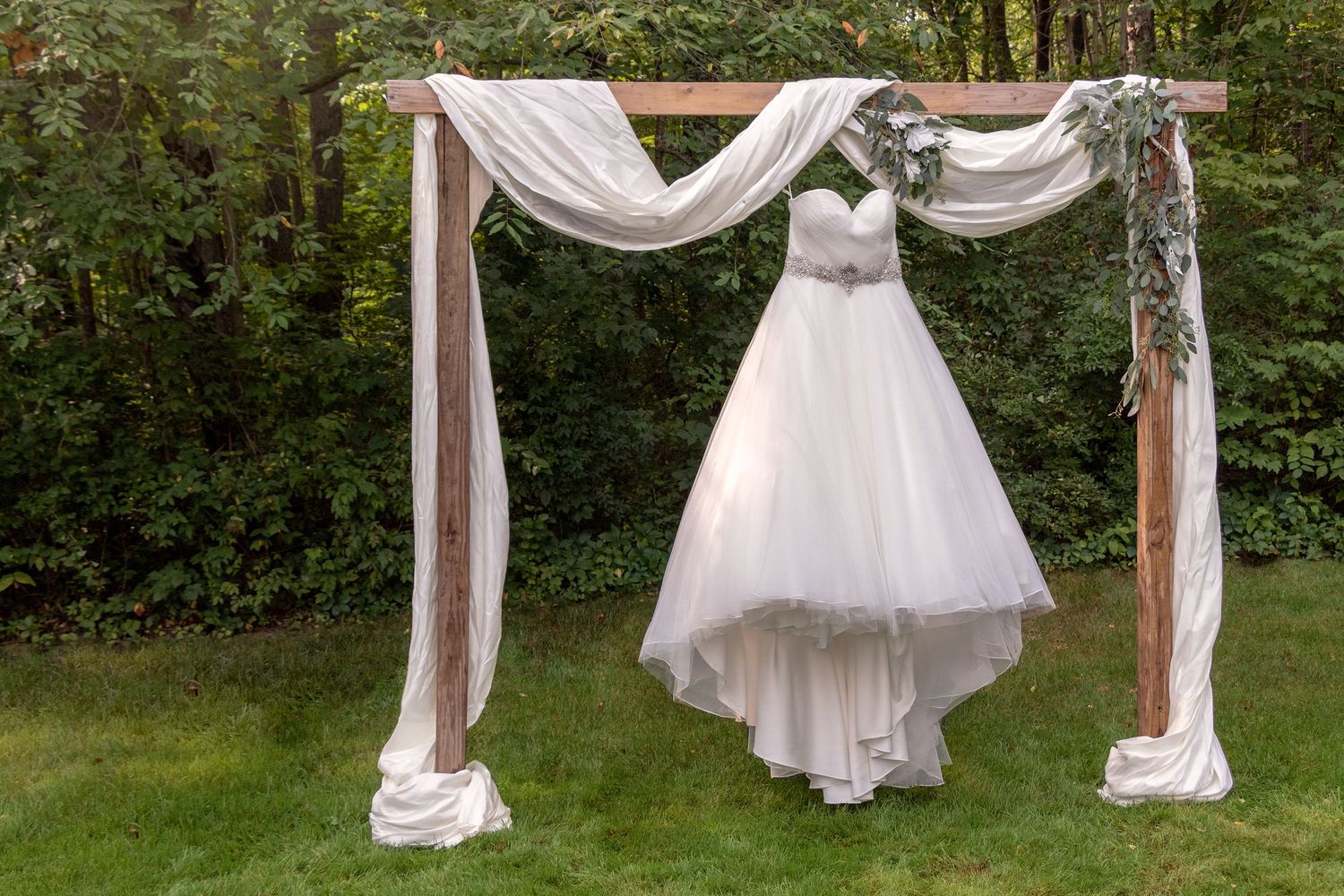 Wedding ceremony site with white fabric draped arch in natural outdoor setting.