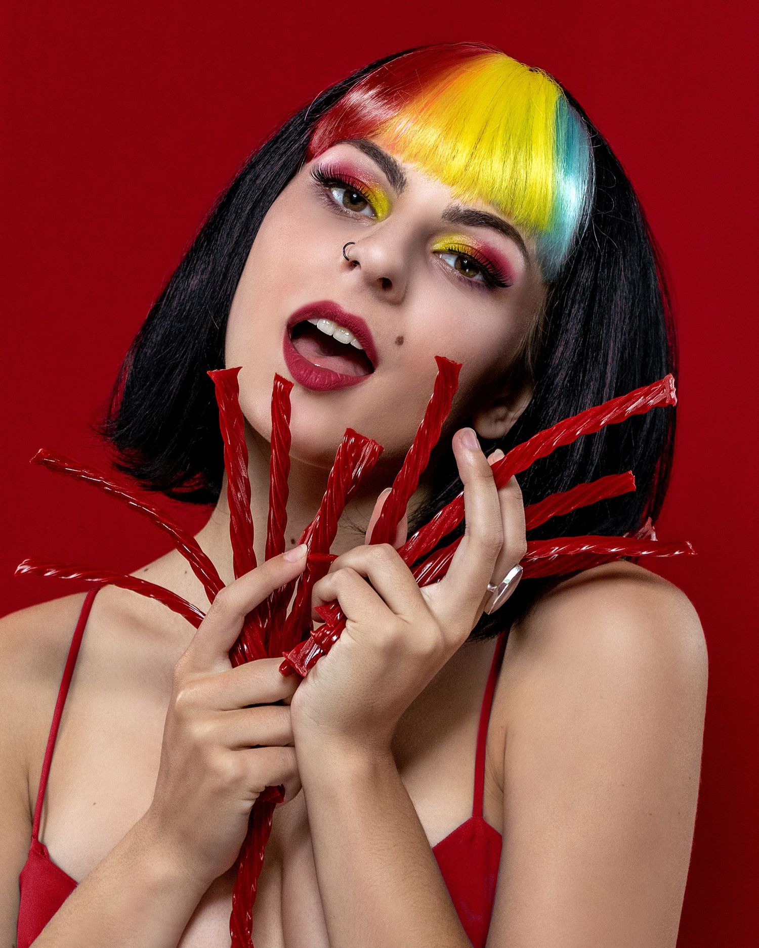 Dramatic portrait with yellow and black hair against red background with red nail extensions.
