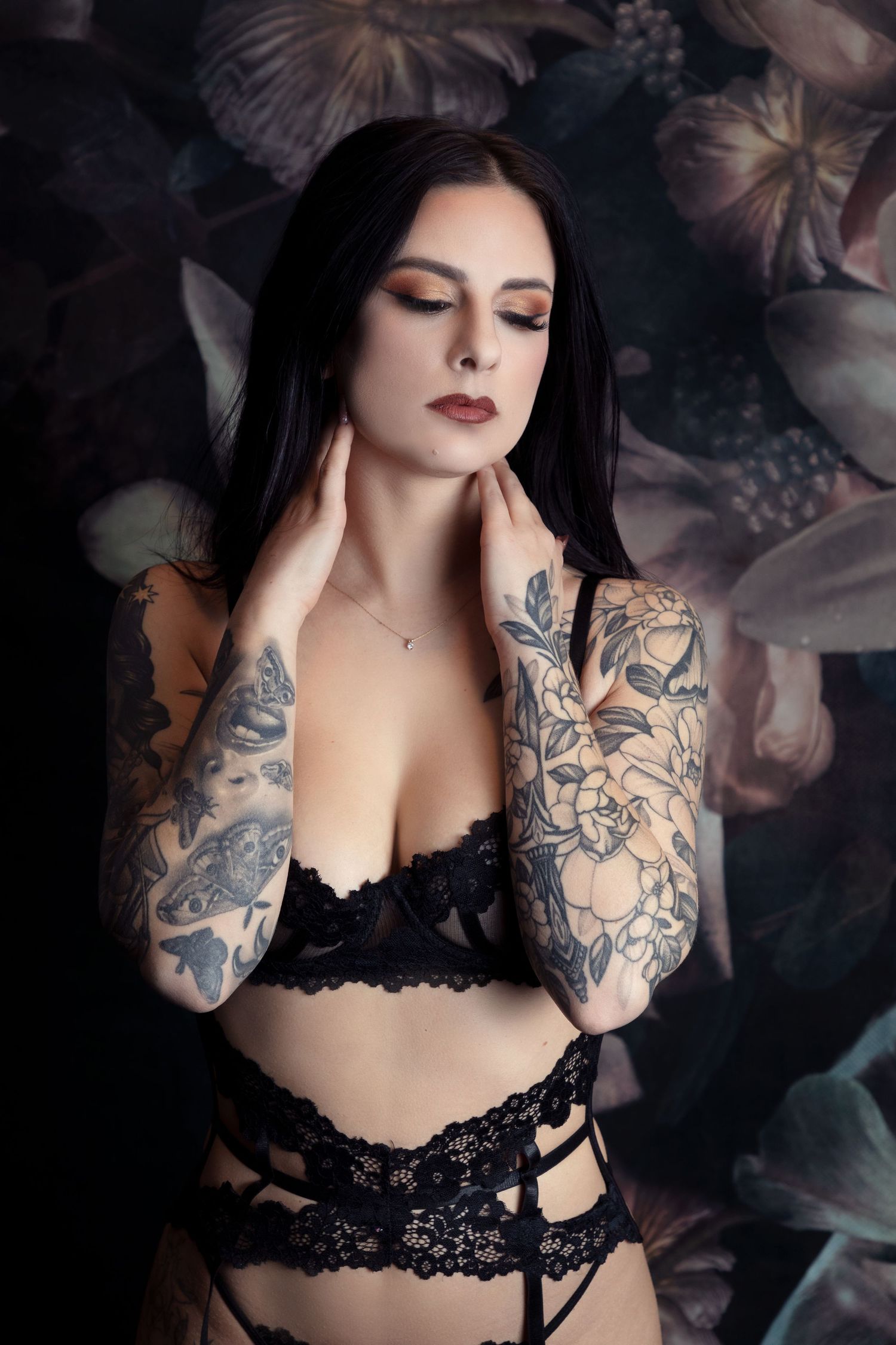 Moody boudoir photography with dark floral backdrop and black lace lingerie.