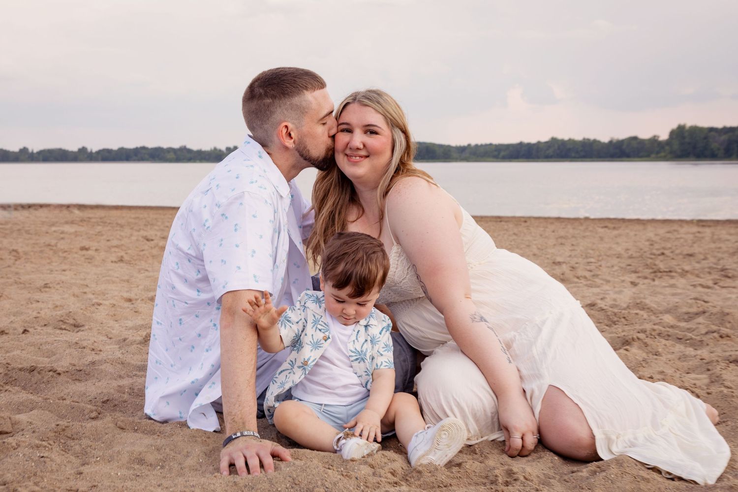 A family enjoying a relaxed photoshoot on a sandy beach at sunset.