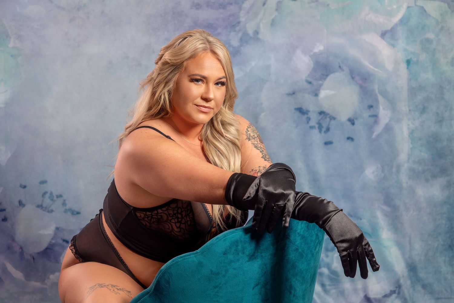 Artistic boudoir portrait with black lingerie against blue watercolor backdrop.