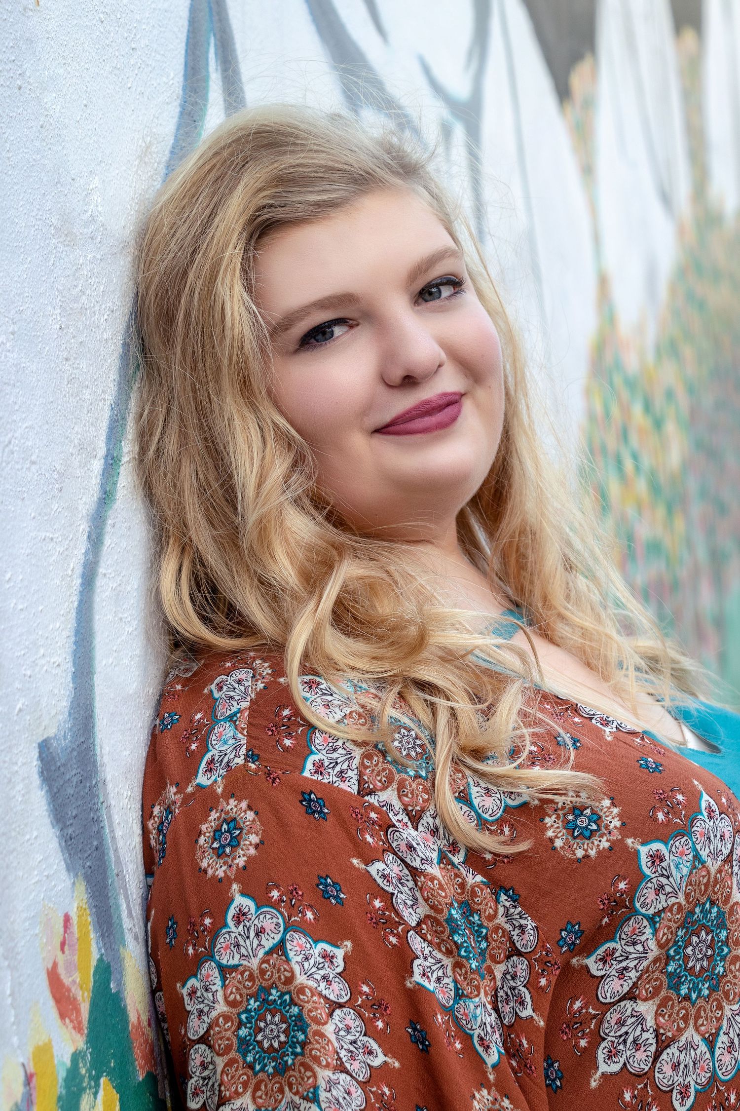 Portrait against white wall wearing brown floral print top with blonde wavy hair.