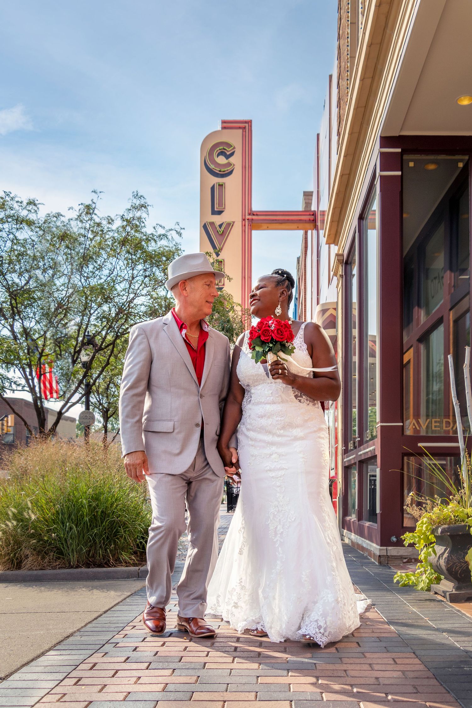 A couple in wedding attire poses outside a historic city theater.