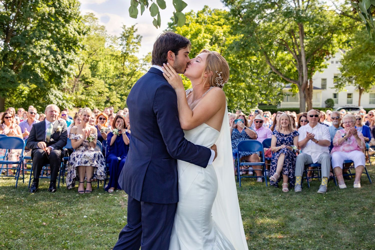 Newlyweds share their first kiss as guests watch during an outdoor garden ceremony.