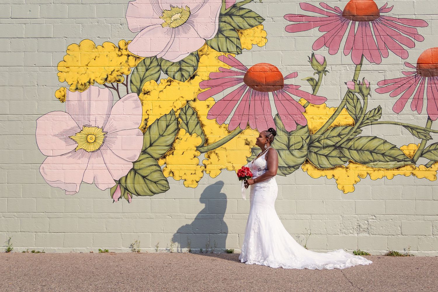 A bride in white poses against a colorful floral mural painted on a brick wall.