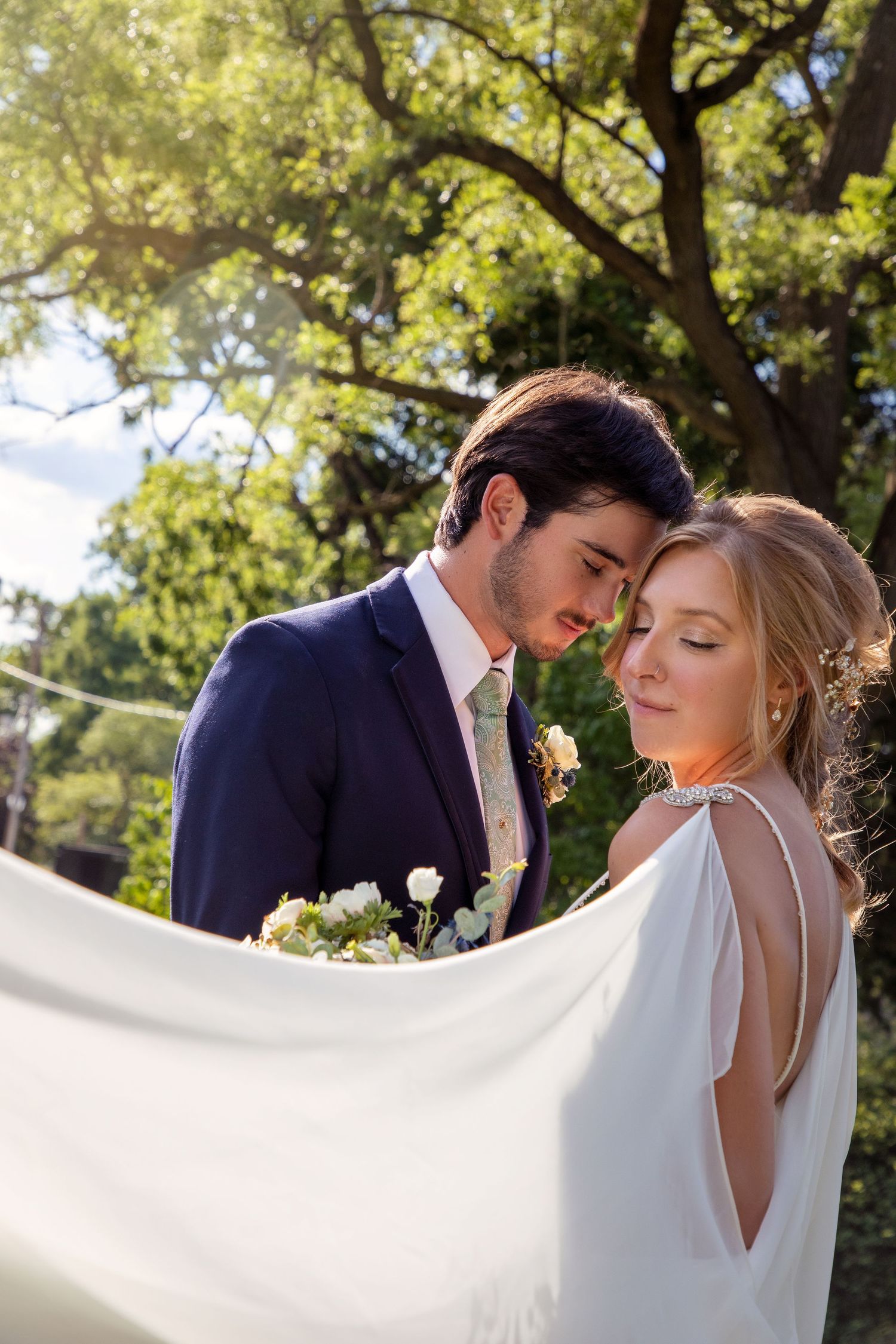 Romantic wedding portrait with flowing dress captured under sunlit trees.